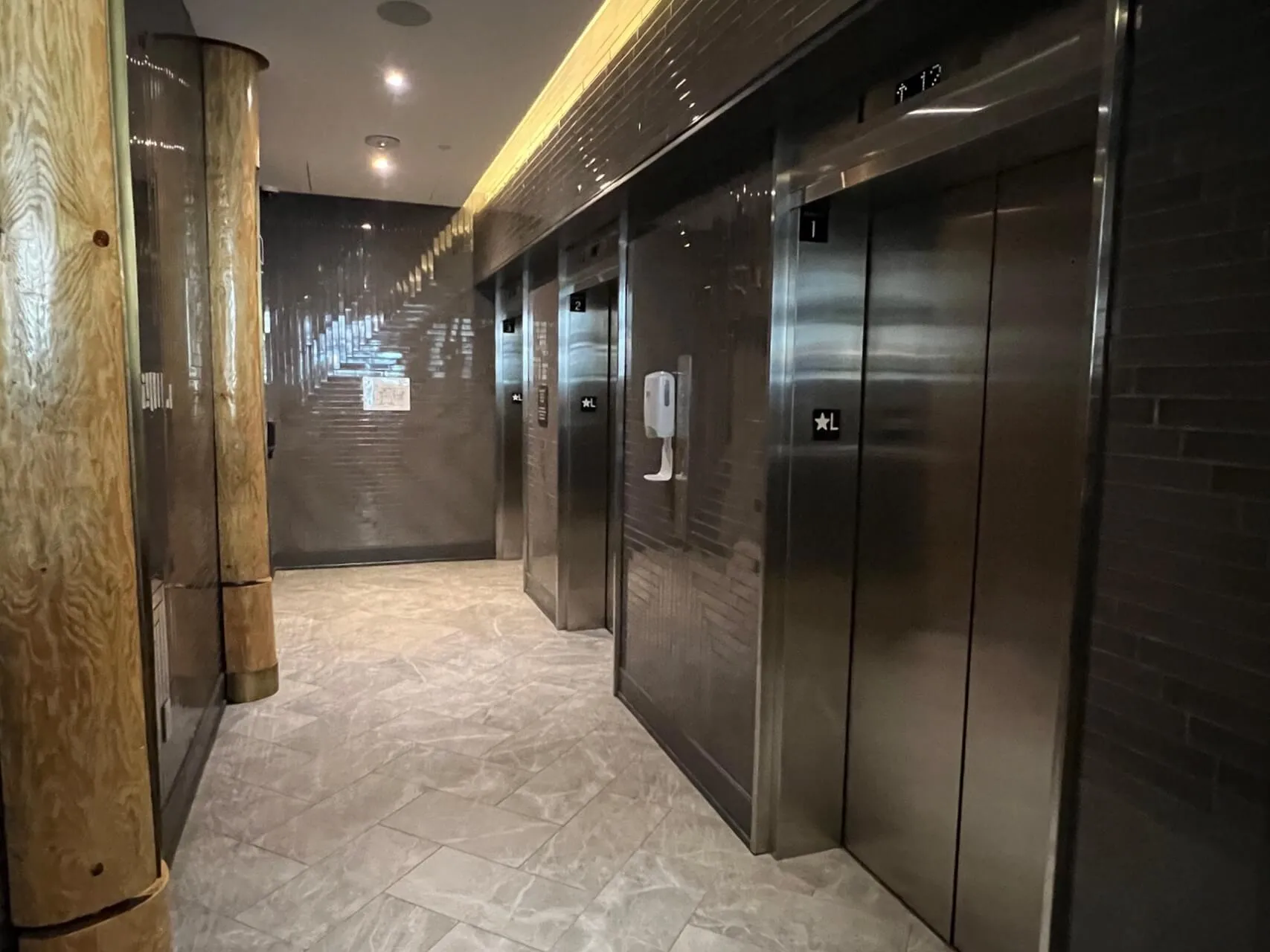 Hotel elevator bank with stainless steel doors in a modern corridor with marble flooring and linear ceiling lights