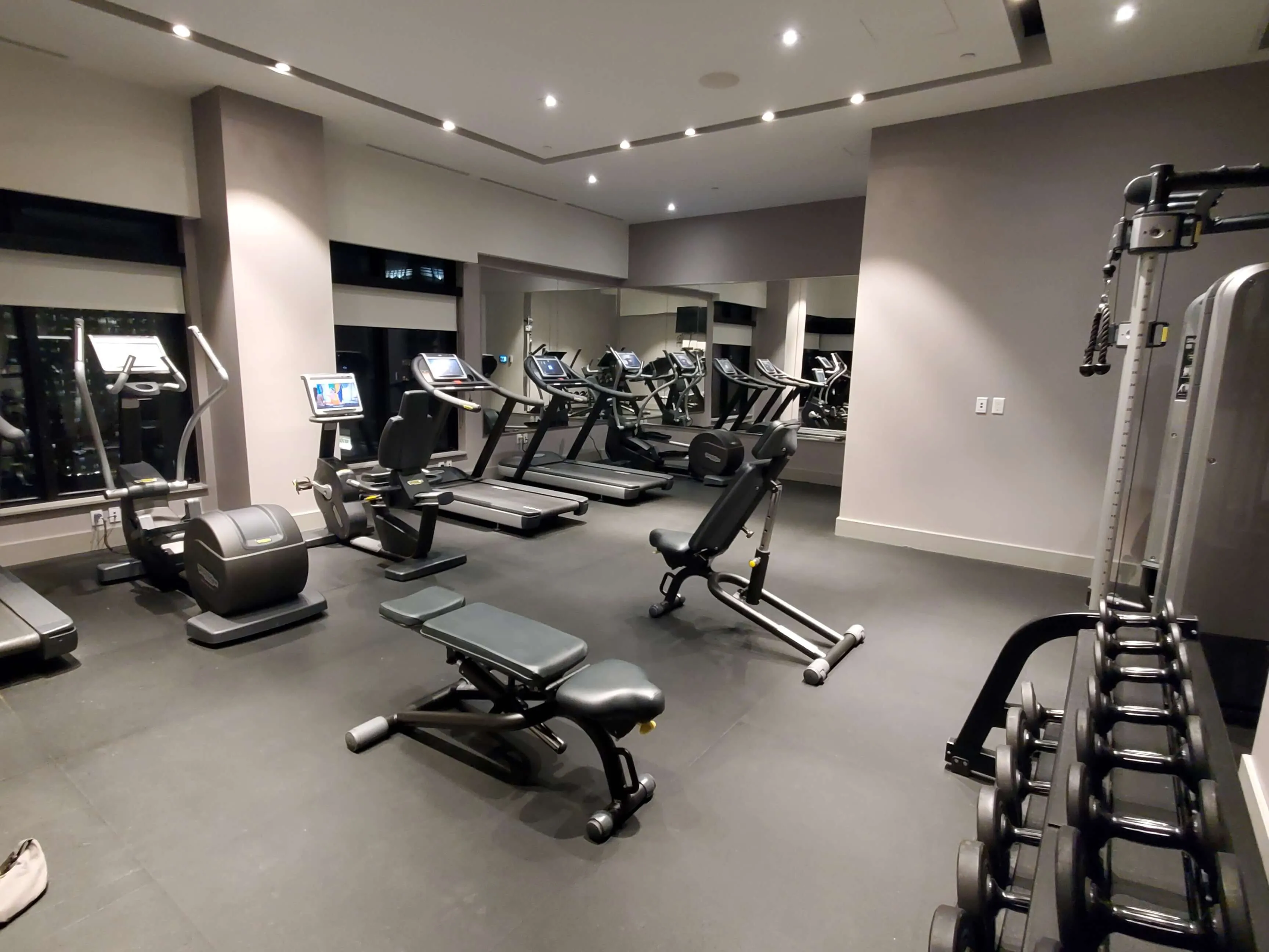 Modern hotel fitness center with treadmills, exercise bikes, weight bench, and dumbbell rack under recessed lighting