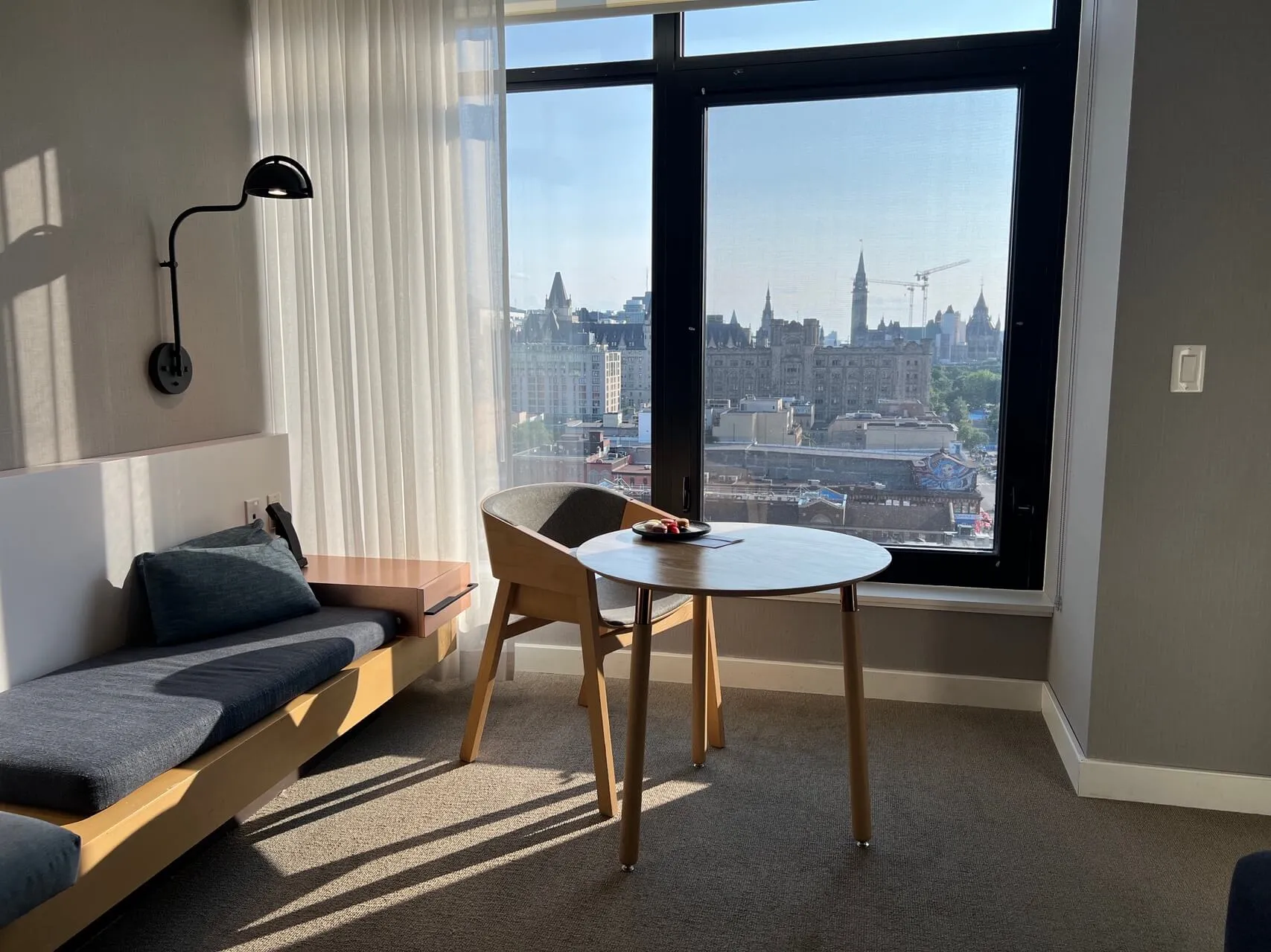Living room with daybed, round white table, and floor-to-ceiling windows overlooking Parliament Hill and Ottawa skyline
