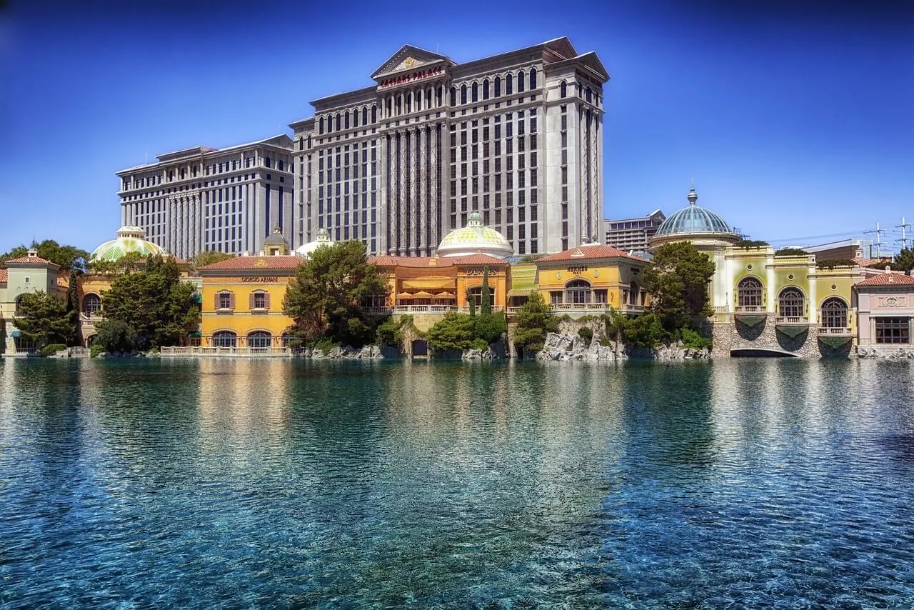 Caesars Palace hotel and casino waterfront facade with yellow and cream-colored buildings reflected in turquoise water under clear blue sky