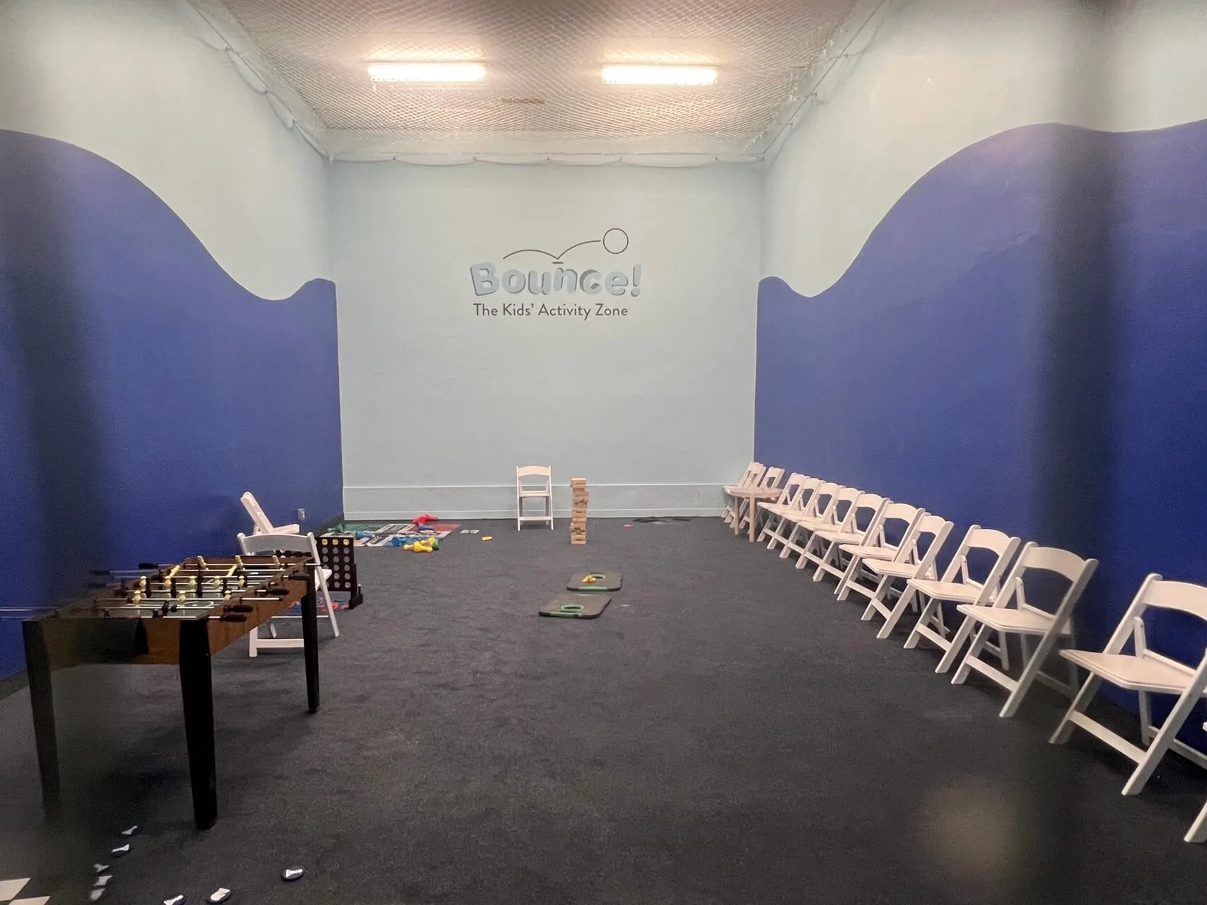 Bounce! Kids Activity Zone with foosball table, toys, and white folding chairs against blue wavy walls