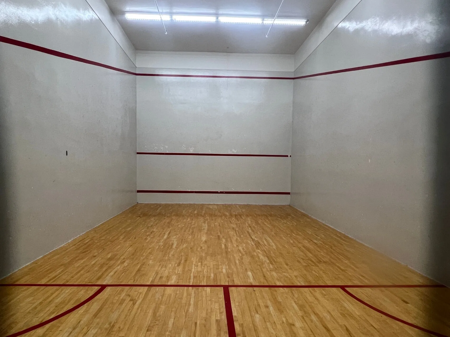 Empty squash court with wooden floor, white walls, and burgundy lines at Delta Hotels Ottawa.