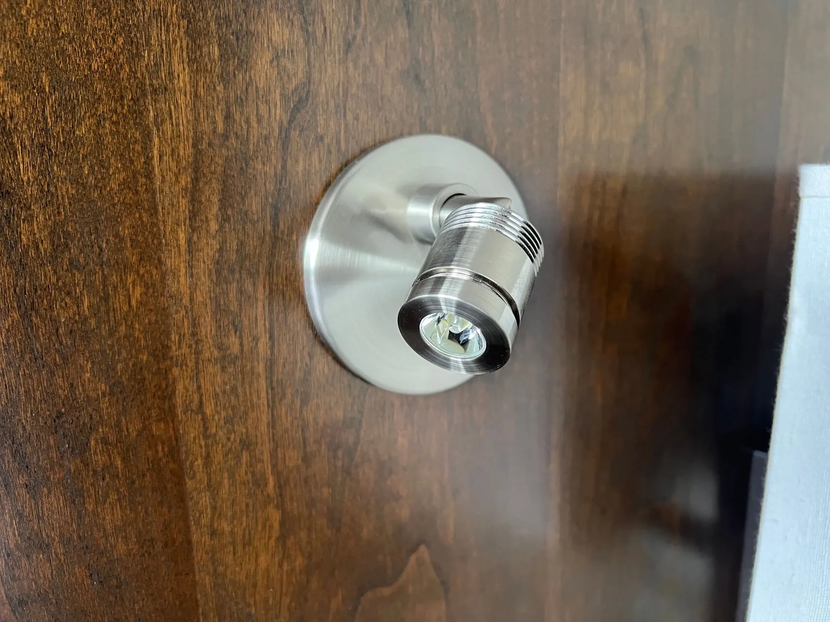 Modern chrome wall-mounted reading lamp on dark wood paneling in aircraft cabin.