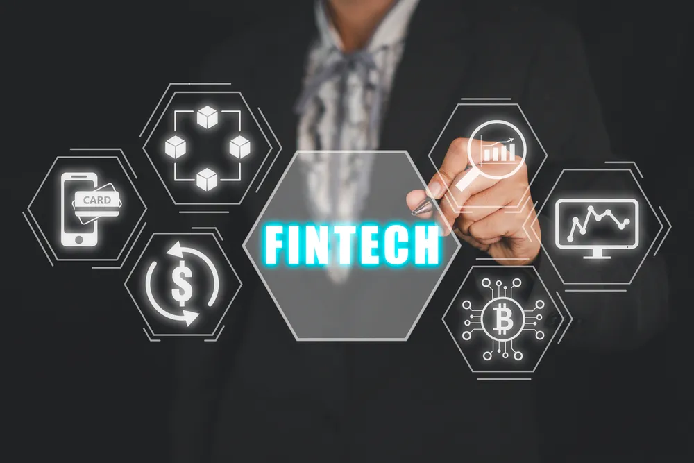 Person in business attire touching holographic FINTECH interface with financial icons including credit card, blockchain, currency, cryptocurrency, and analytics symbols