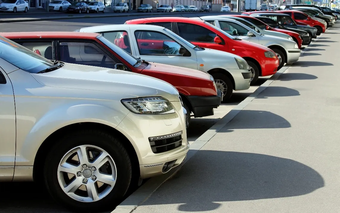 Row of parked rental cars in various colors including white, red, and cream on a sunny day in a parking lot.