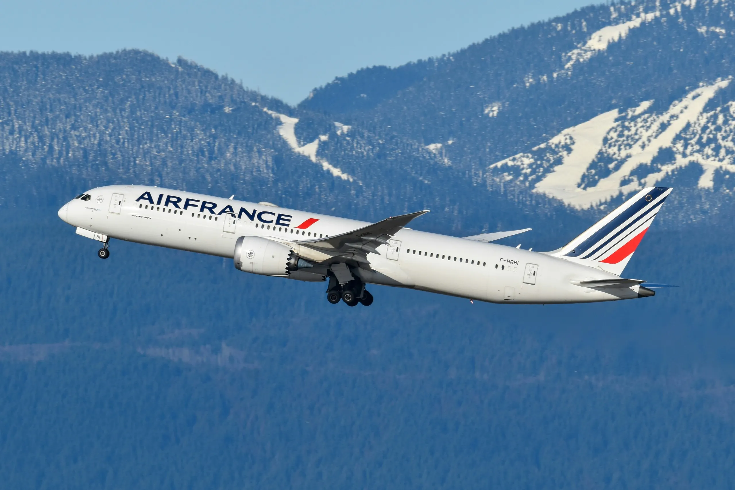 An Air France Boeing 787 departing Vancouver with forested, snow-streaked mountains behind