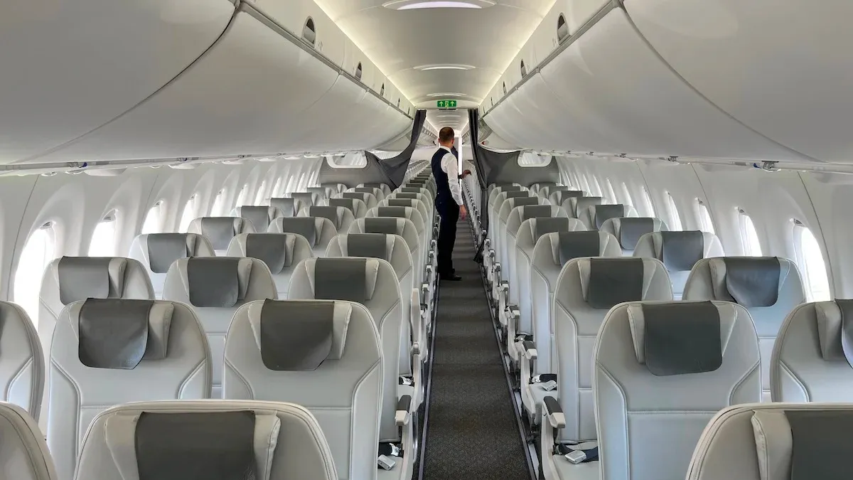 Empty aircraft cabin with rows of white seats and emergency exit sign visible down the aisle