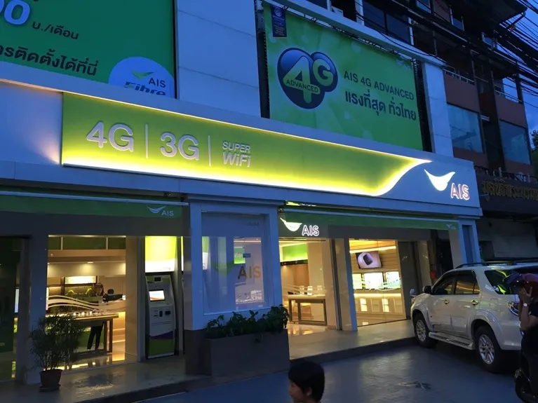 AIS storefront in Thailand at dusk with 4G and 3G signage, blue and green illuminated facade.