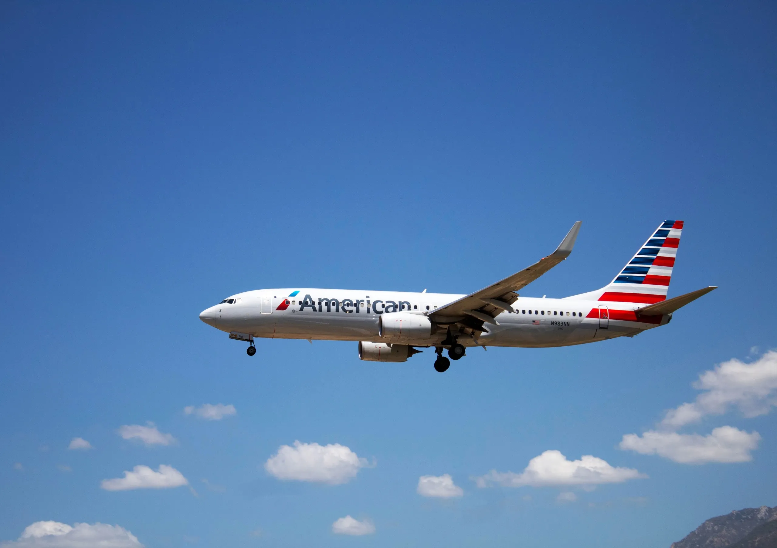 An American Airlines Boeing 737 flying against a blue sky with scattered clouds