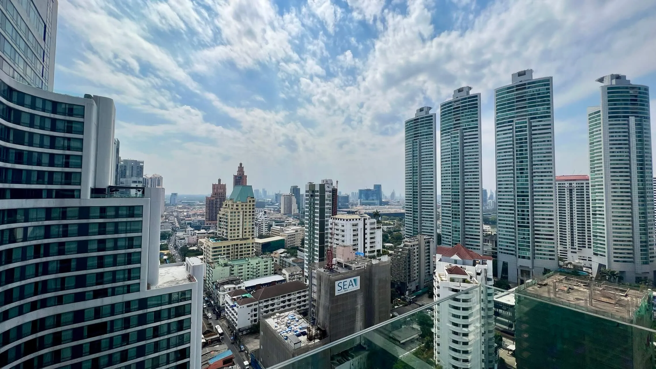 Bangkok cityscape with mix of modern high-rise condos and older mid-rise buildings under blue sky with clouds