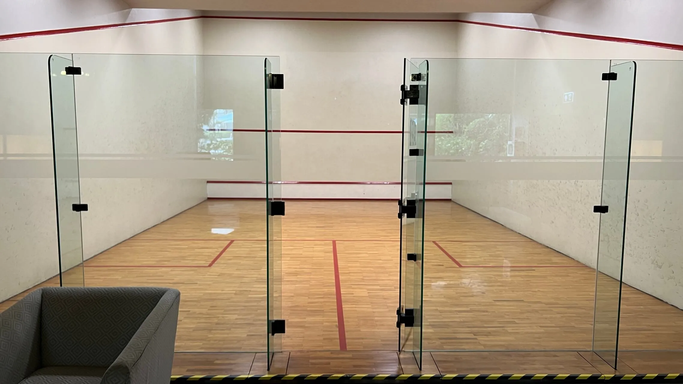 Empty squash court with glass walls, wooden floor, and red court markings at Bangkok Marriott Marquis