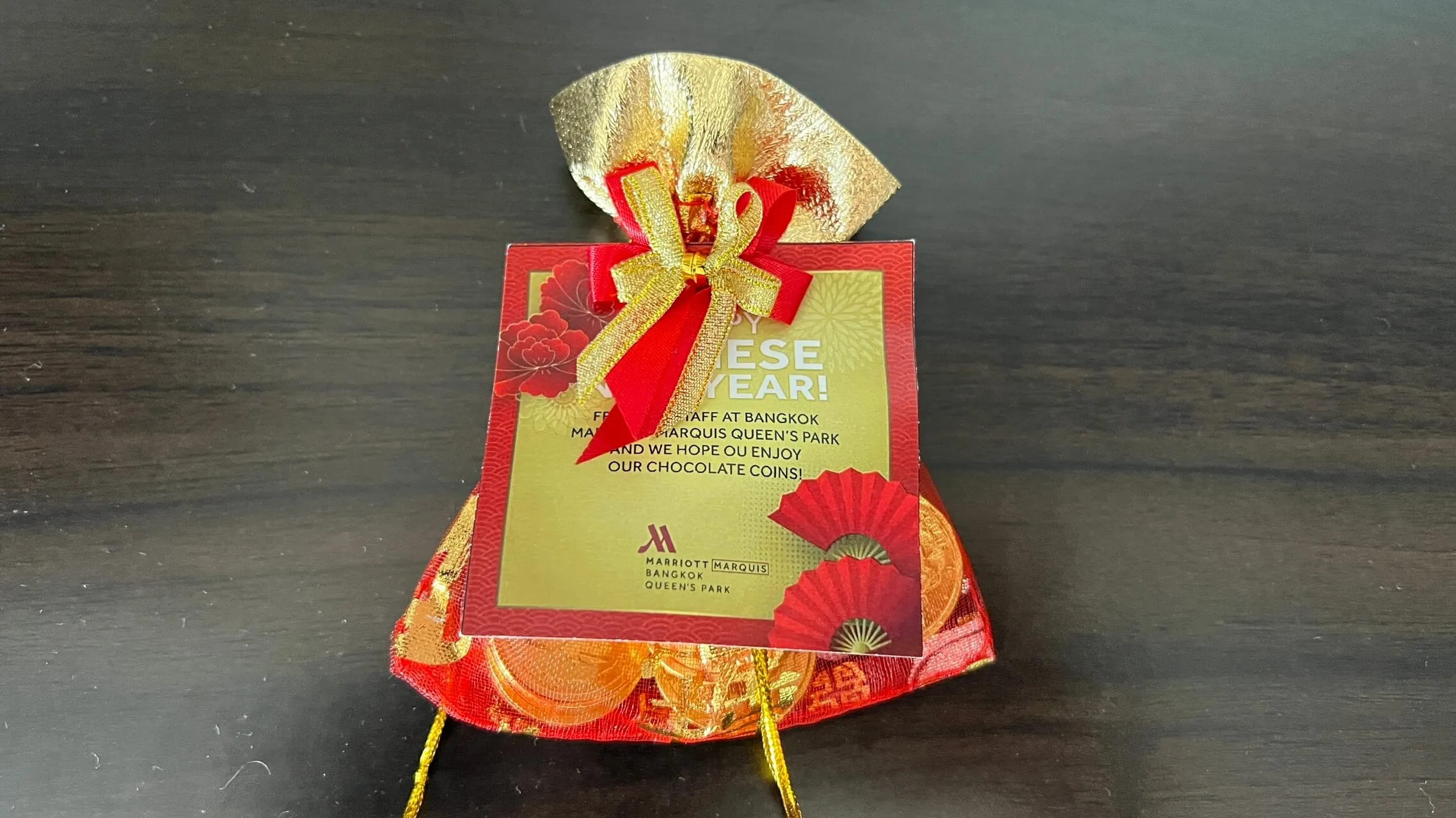 Red and gold Lunar New Year gift bag from Marriott Marquis Bangkok Queen's Park with decorative ribbon bow.