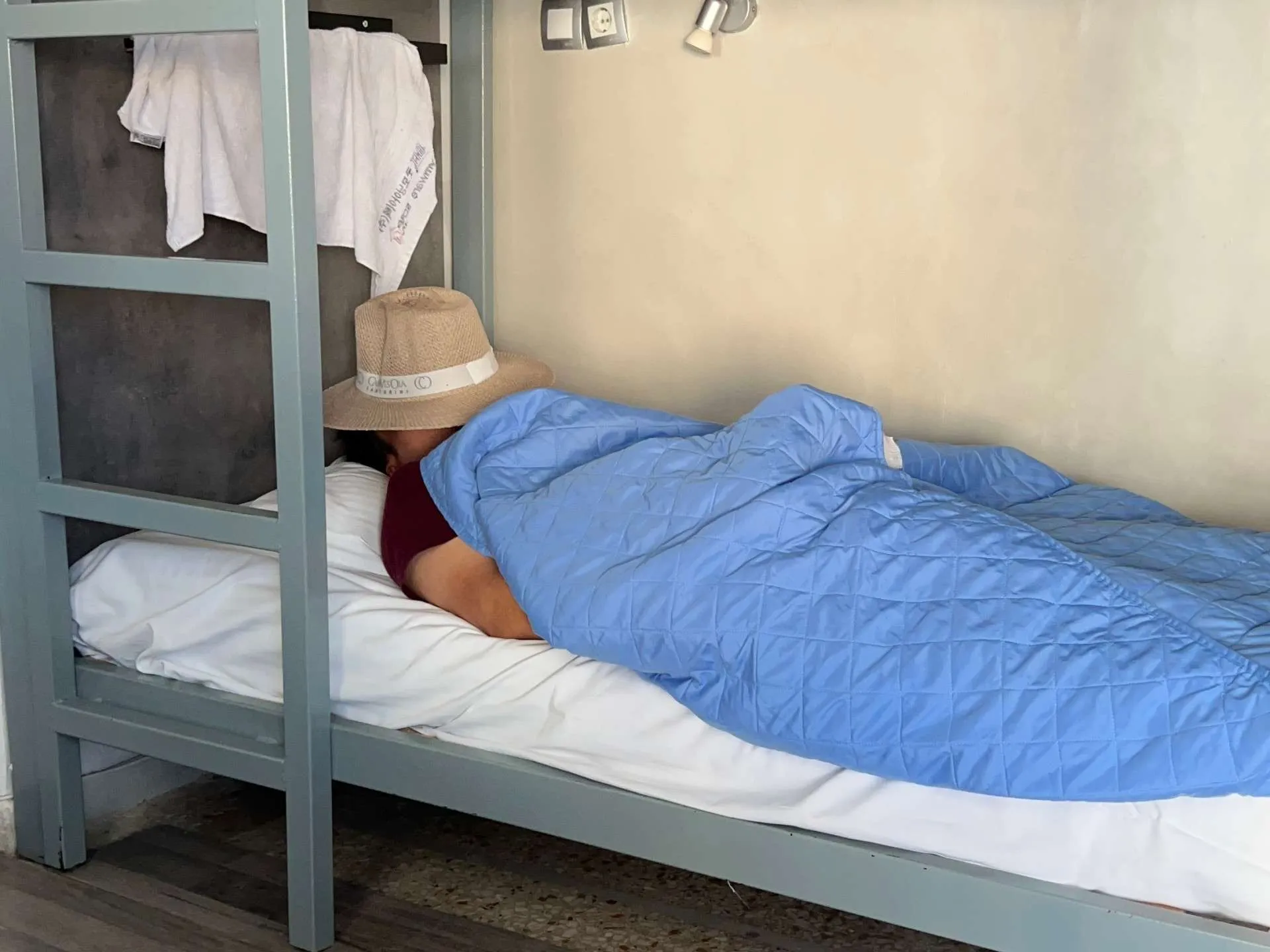 Person sleeping in bunk bed with blue duvet at Bedbox Athens hostel