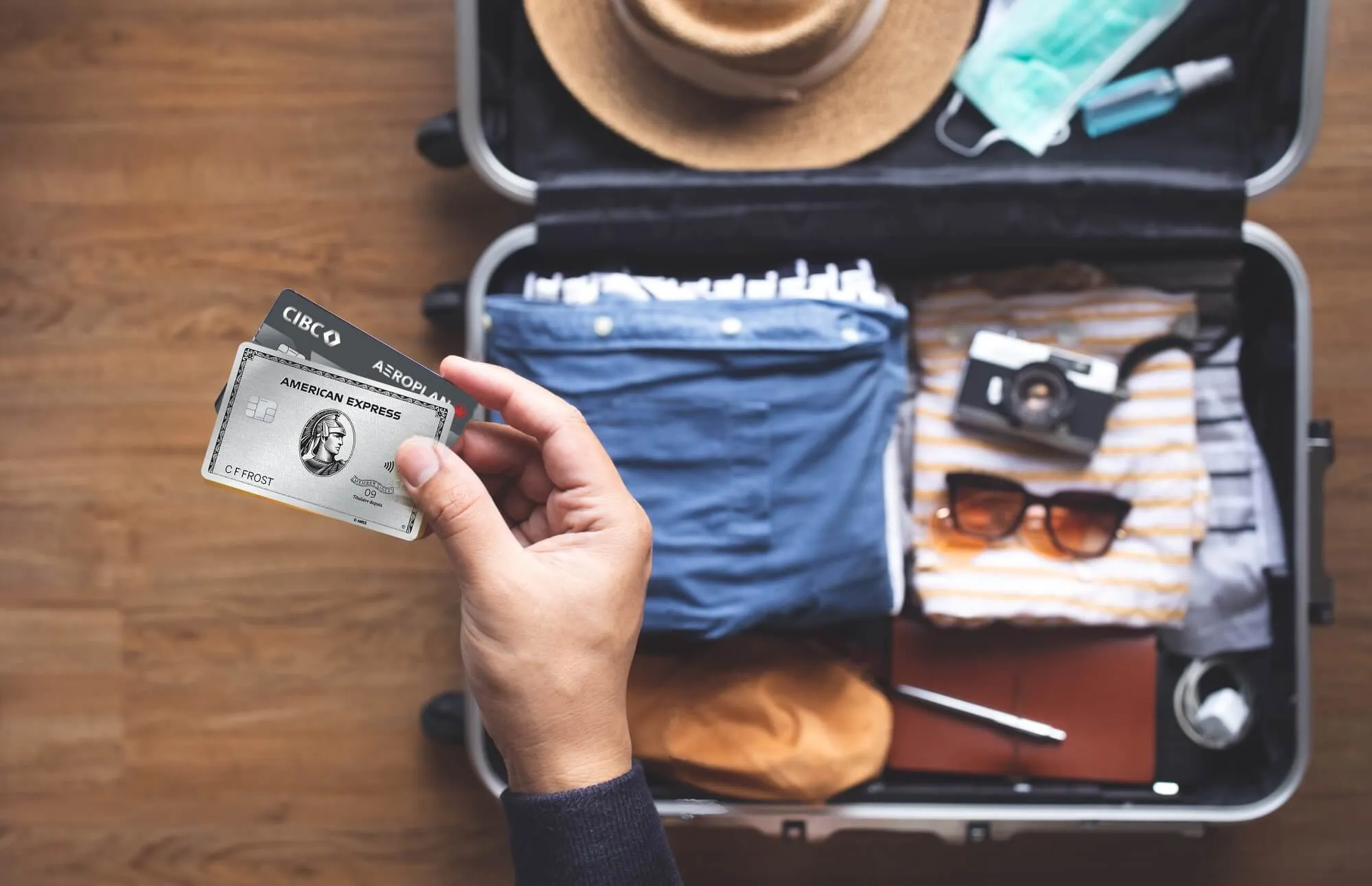 American Express Centurion Card held over open suitcase with travel essentials including sunglasses, hat, and clothing