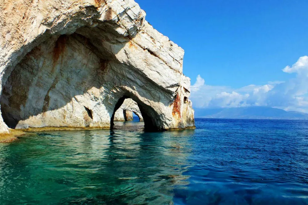 White limestone sea caves with natural arch opening over turquoise and blue Mediterranean water, Zakynthos