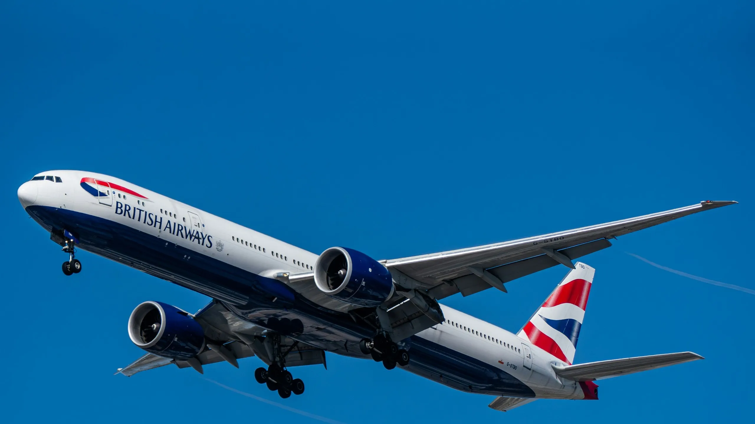 A British Airways Boeing 777-300ER on final approach against a clear blue sky