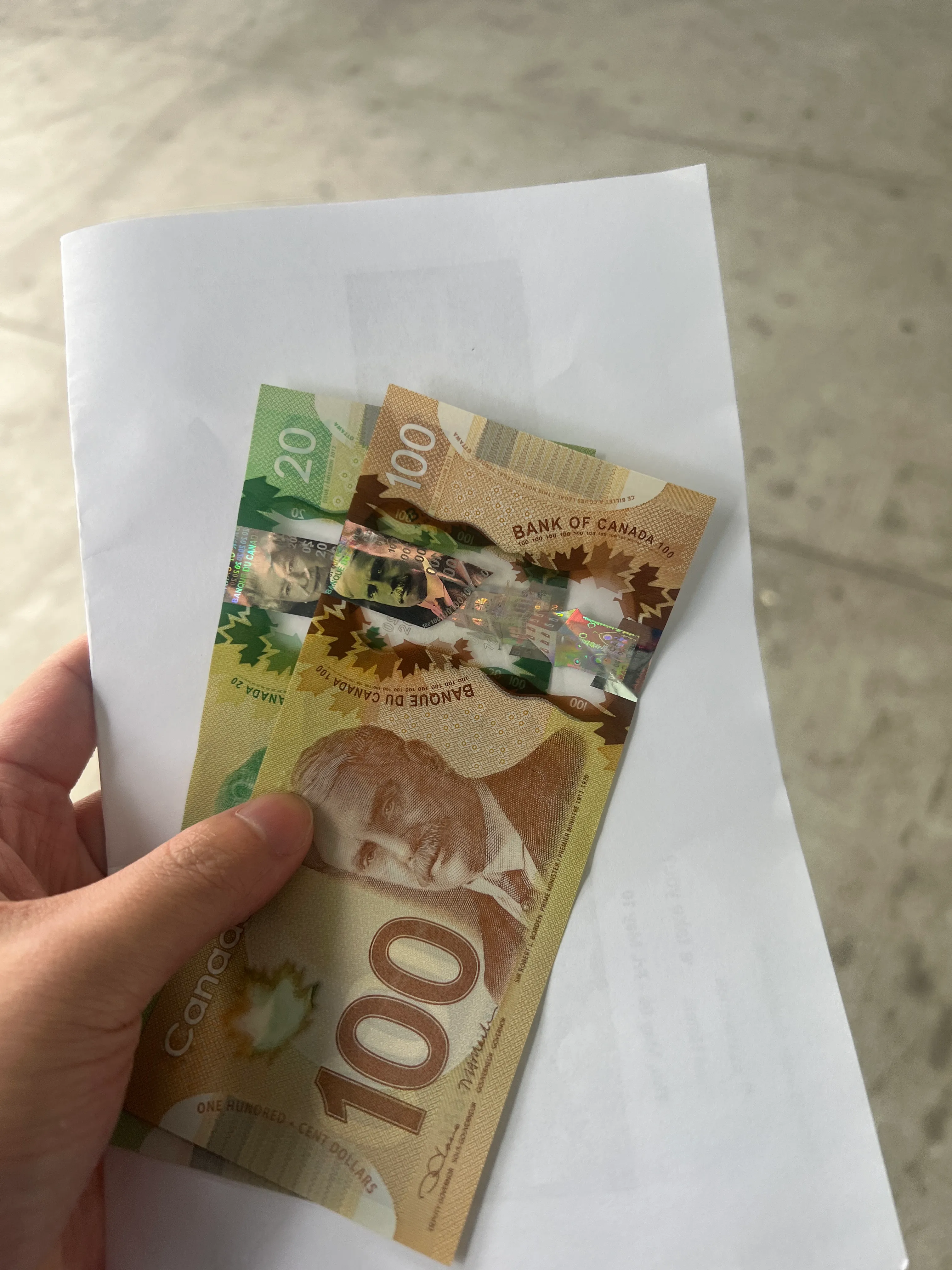 Canadian banknotes ($20, $100) fanned out in hand over white paper, marble surface background