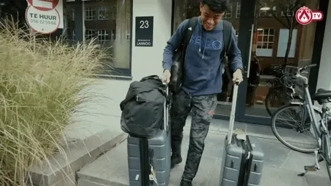 Traveler with roller luggage and backpack standing on street outside a building with Te Huia sign visible