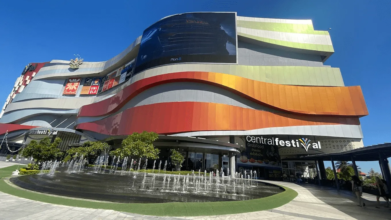 Central Festival Chiang Mai shopping mall exterior with distinctive curved wave architecture and colorful bands in red, orange, and yellow against blue sky.