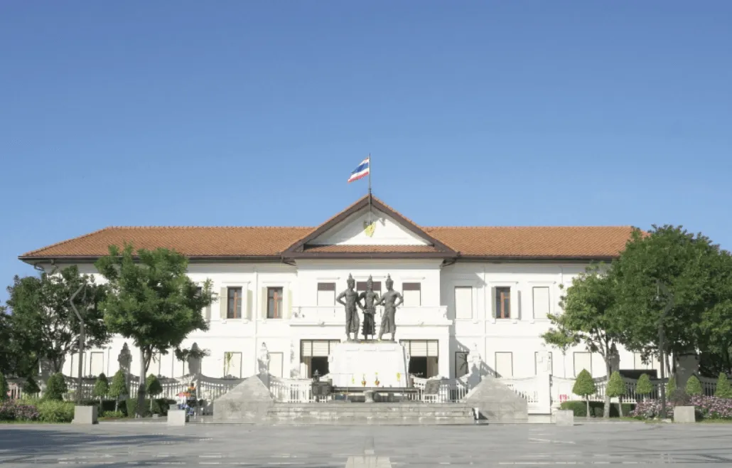 Chiang Mai City Arts and Cultural Center, a white neoclassical building with Thai flag and bronze sculpture, under clear blue sky