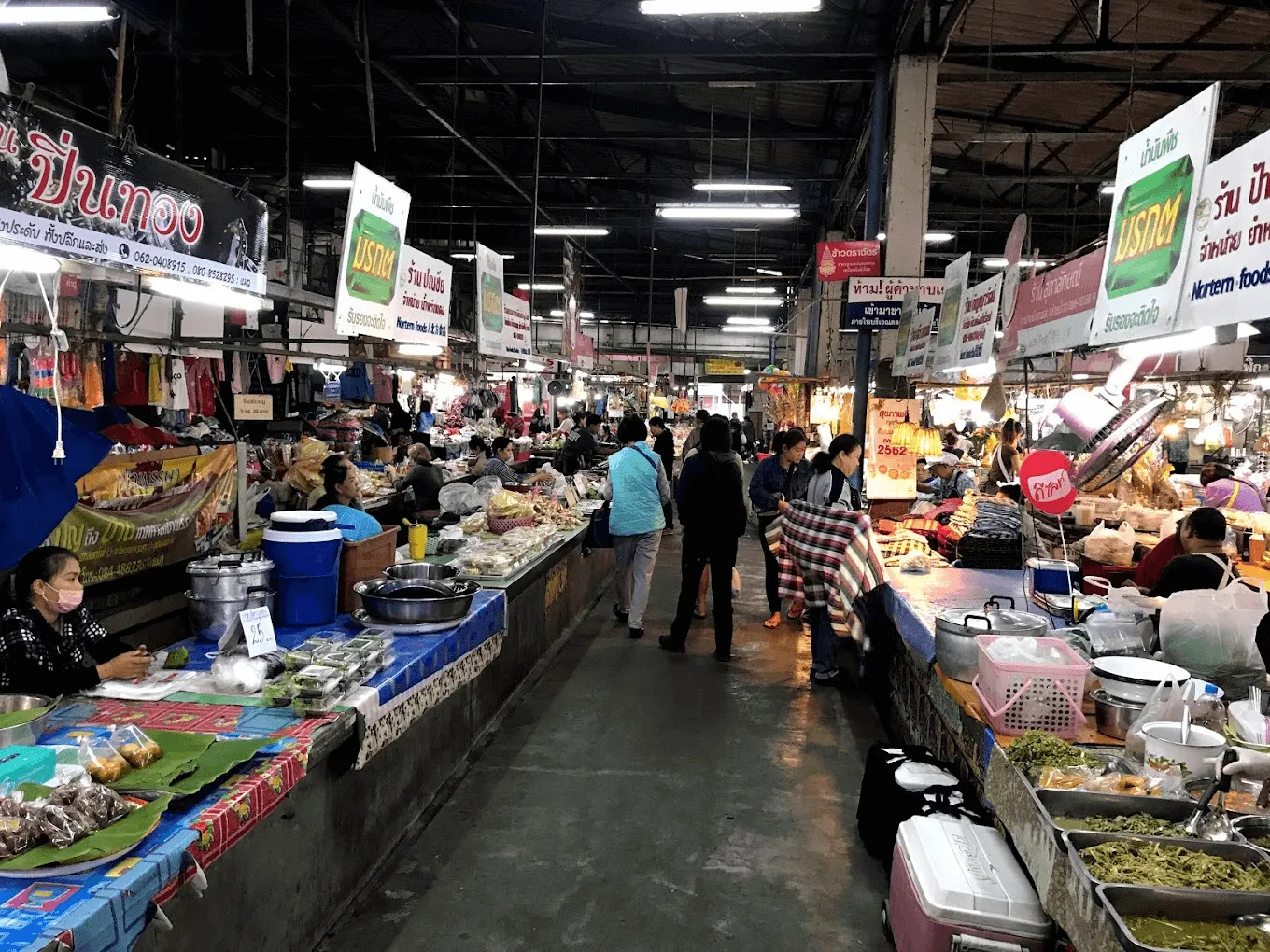 Crowded indoor market hall with produce and food stalls, Thai signage, and shoppers browsing goods at Chiang Mai Gate Market