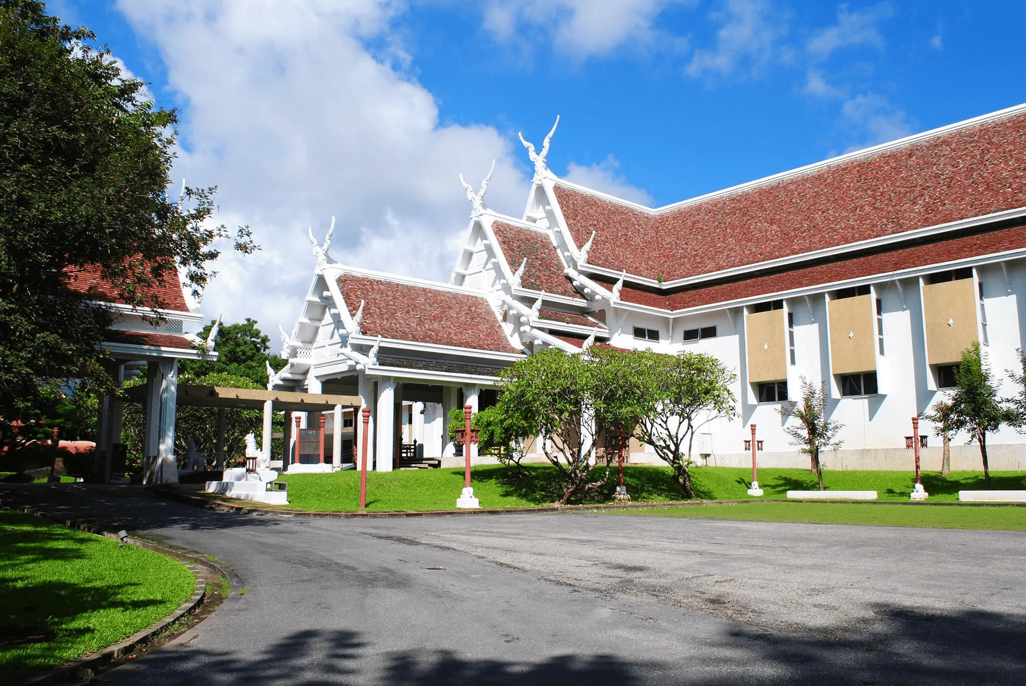 Chiang Mai National Museum exterior with white peaked roofs and terracotta tiles, surrounded by manicured gardens and green lawn under blue sky.