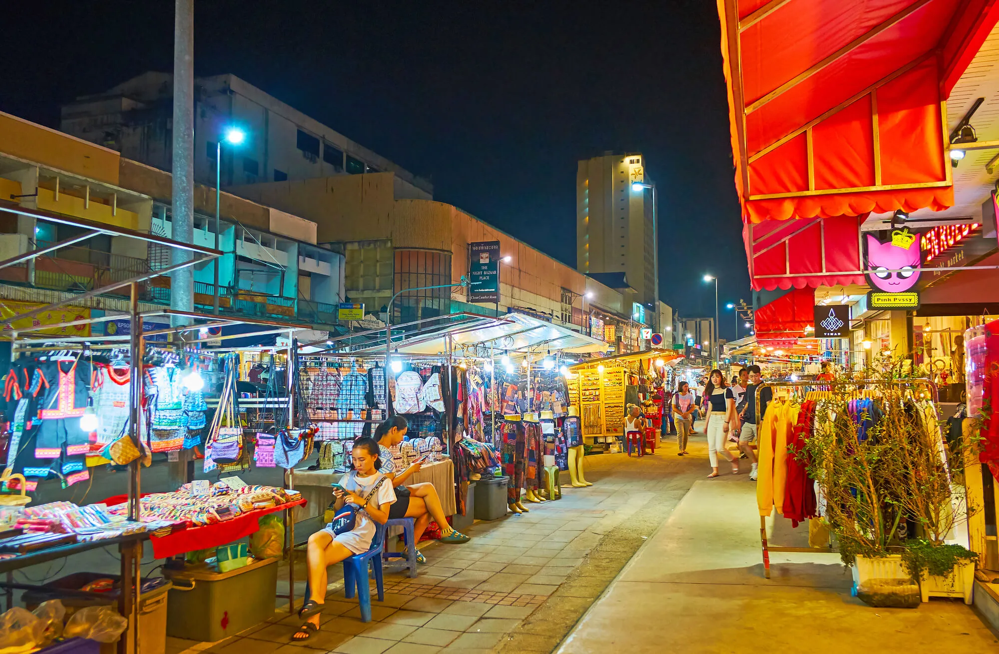 Chiang Mai Night Bazaar with vendor stalls, clothing displays, and red signage under nighttime illumination
