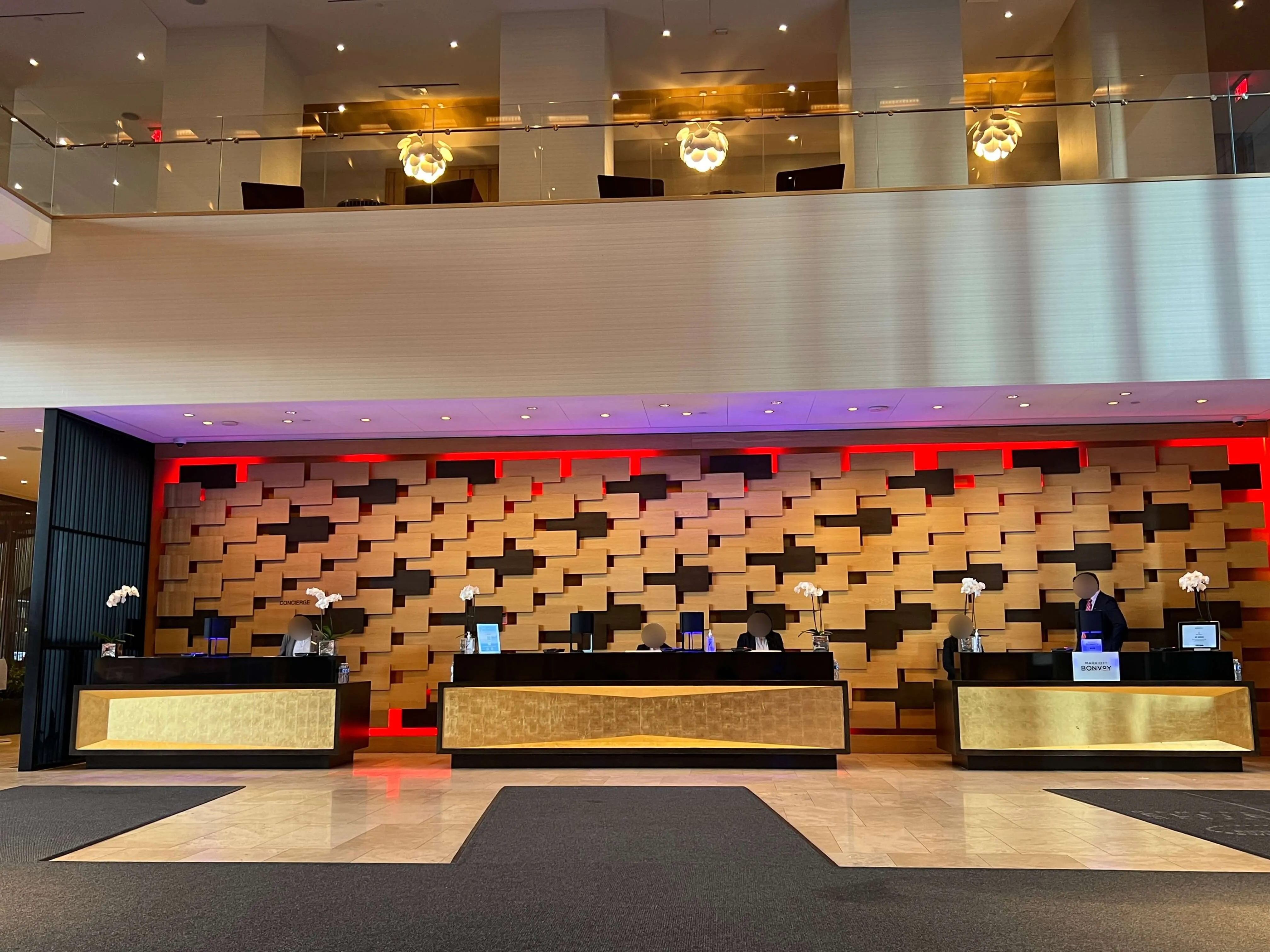 Delta Hotels Toronto front desk with three gold-topped reception counters, textured wood wall feature with red and black accents, and modern lighting.