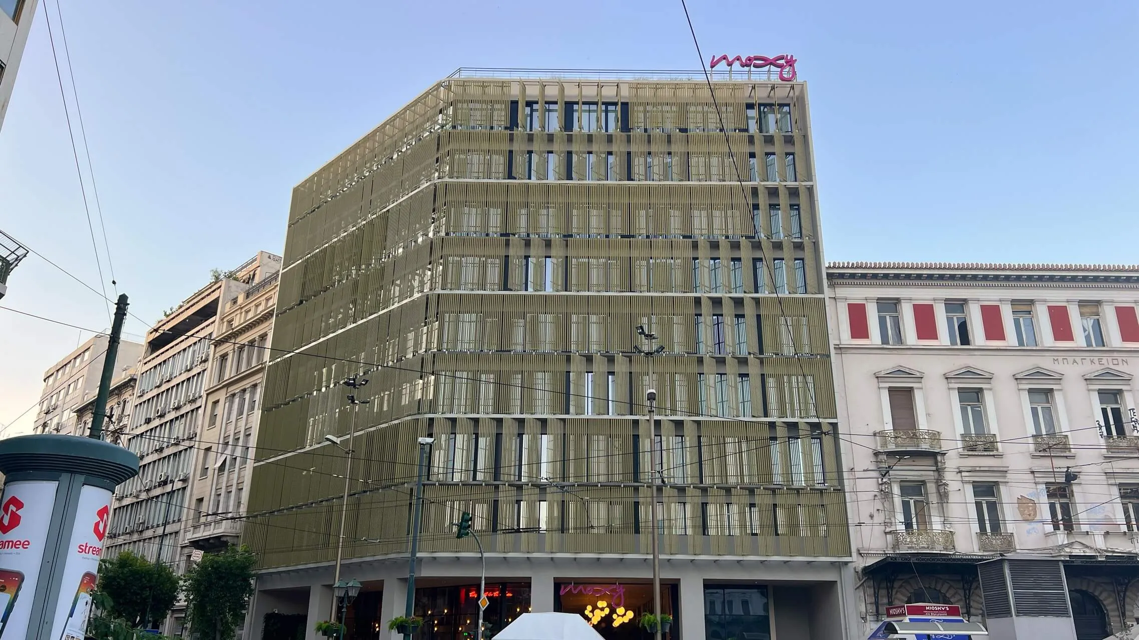Modern mid-rise building with olive-green facade and horizontal window bands on a European city street with classical architecture