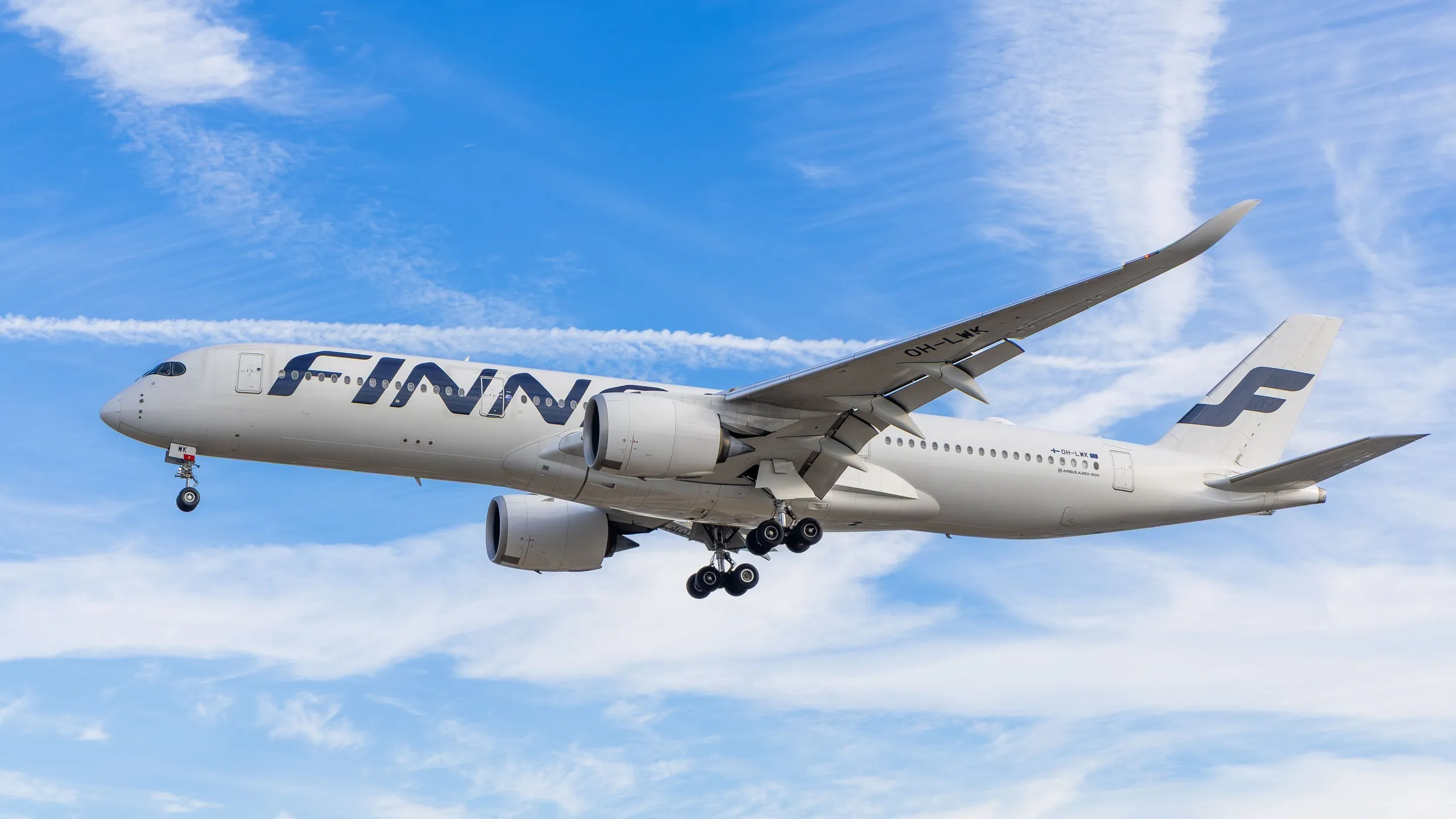 A Finnair Airbus A350 on landing approach against a blue sky with wispy clouds