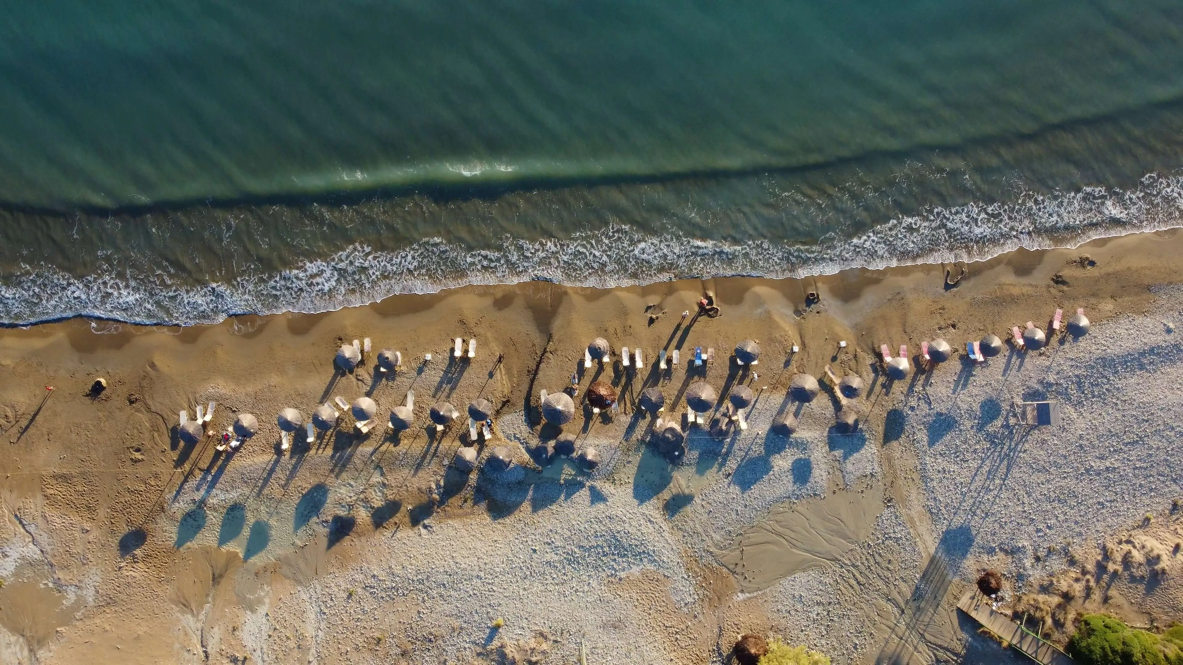 Aerial view of beachgoers scattered along sandy shoreline with turquoise ocean and white-capped waves at Gerakas Beach