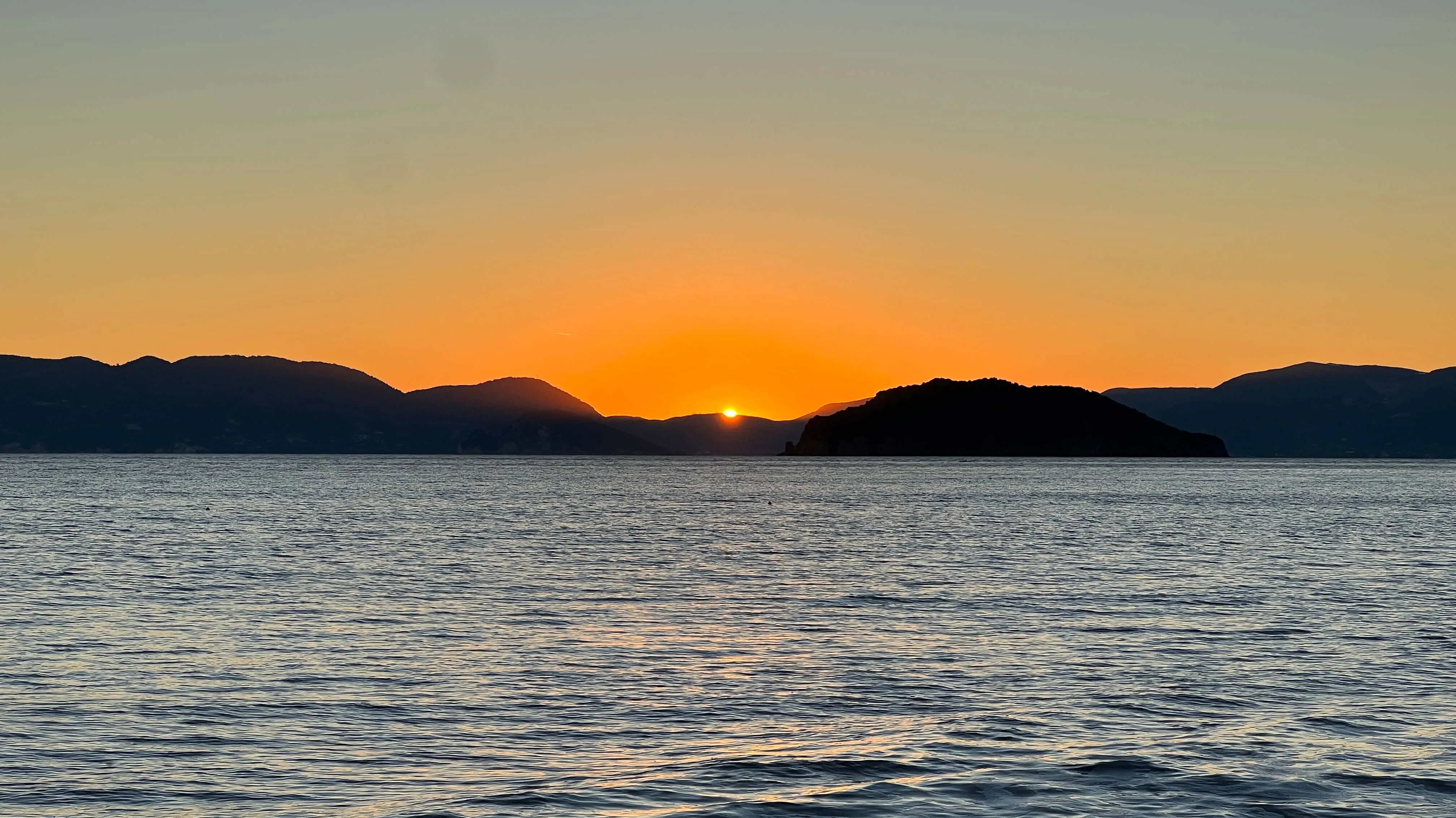 Sunset over Gerakas Bay with mountains silhouetted against golden sky and calm sea.