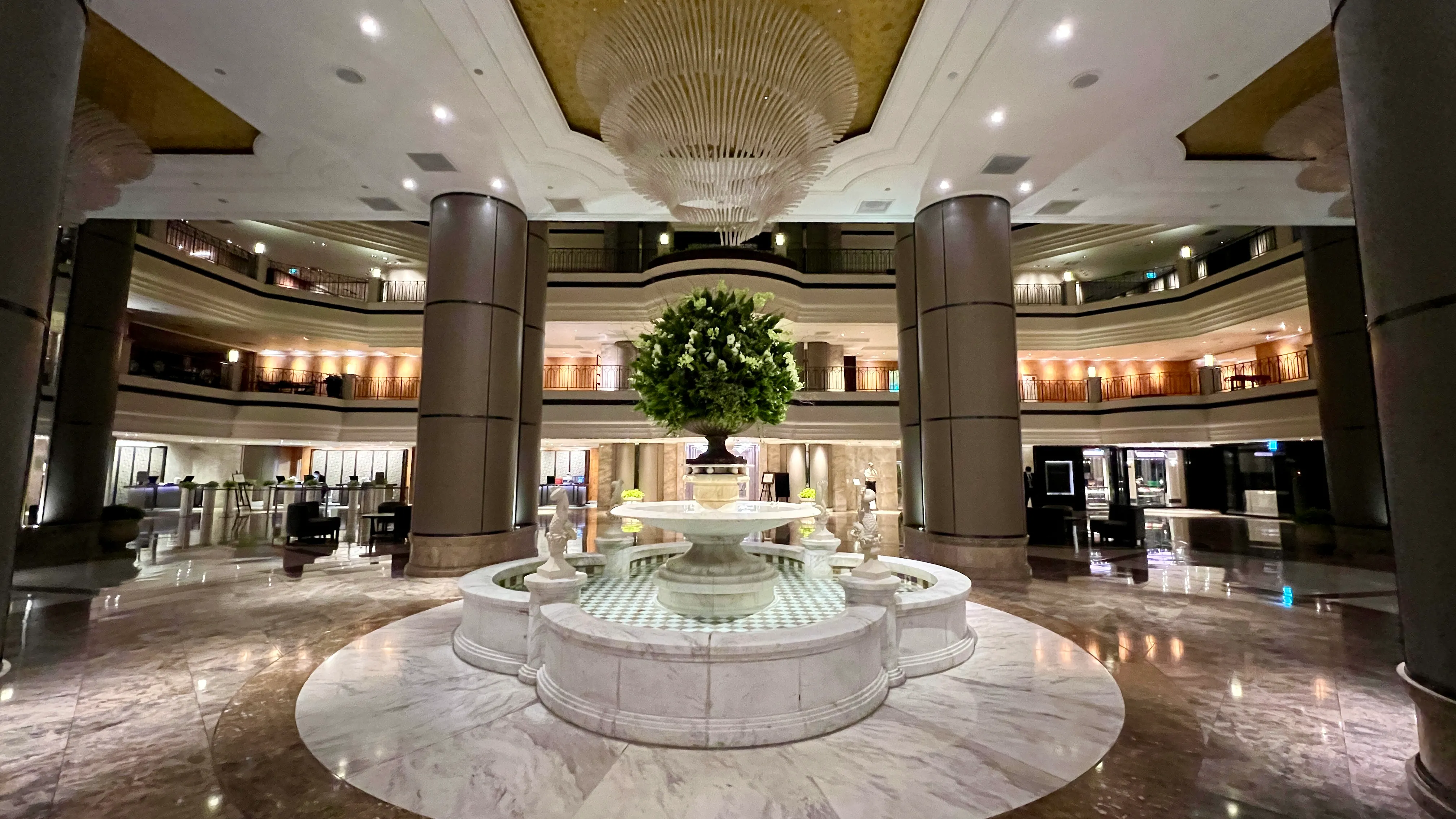 Grand Hyatt Taipei lobby with marble floors, central fountain, soaring columns, and multi-level balconies with ambient lighting.