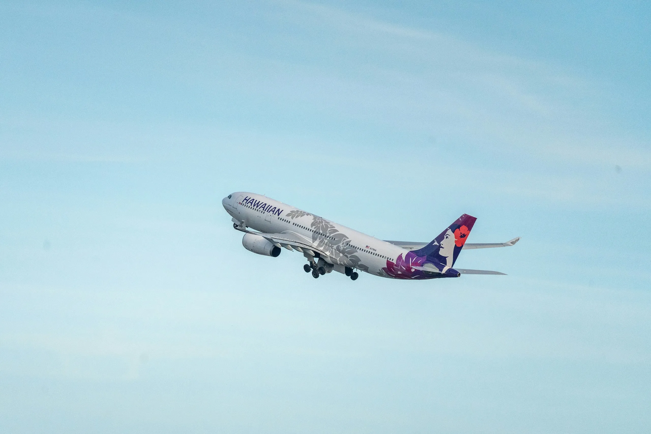 A Hawaiian Airlines Airbus A330 climbing after takeoff against a pale blue sky