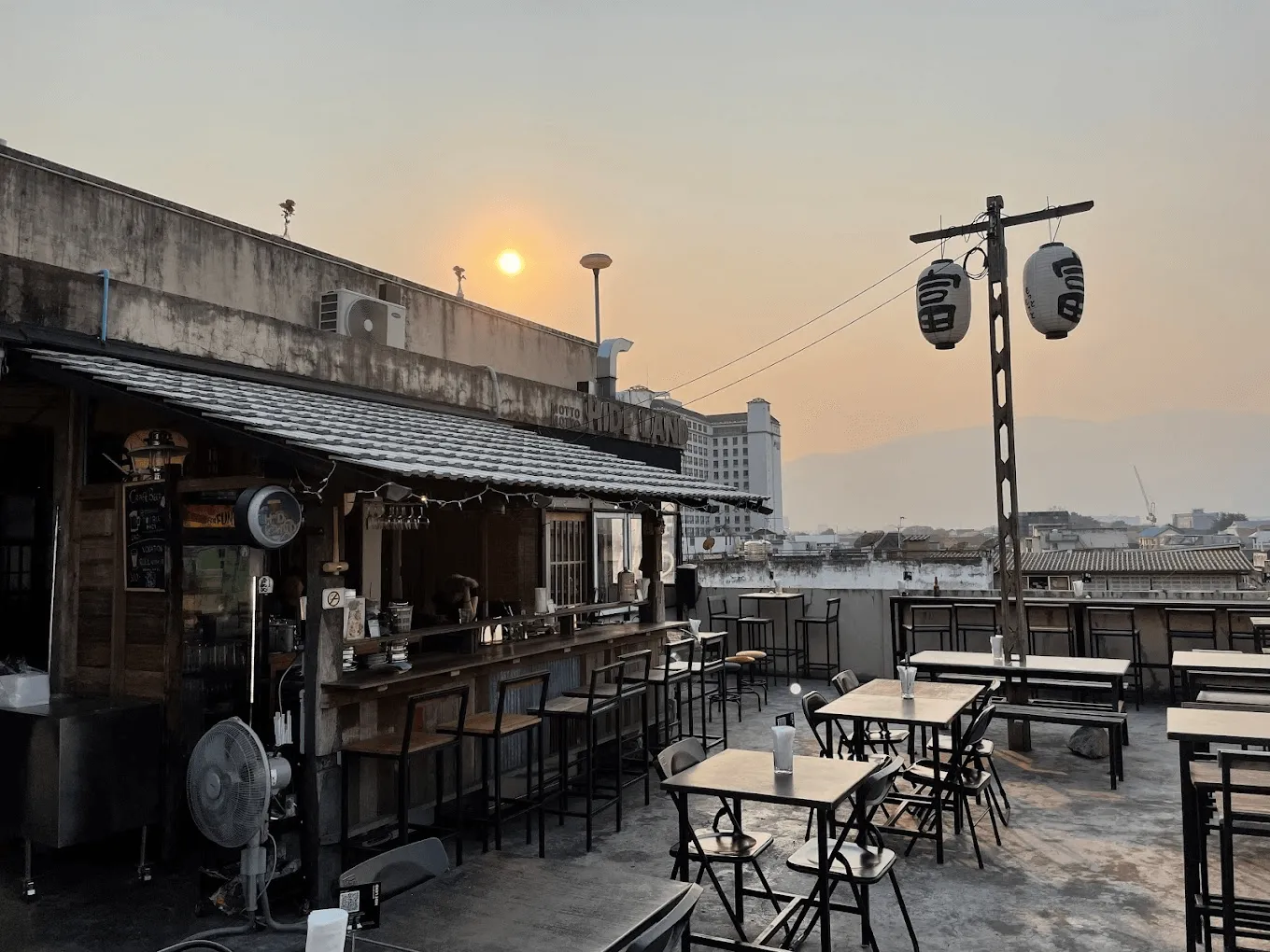Rooftop bar with dark wooden counter and seating, sunset over water and city skyline