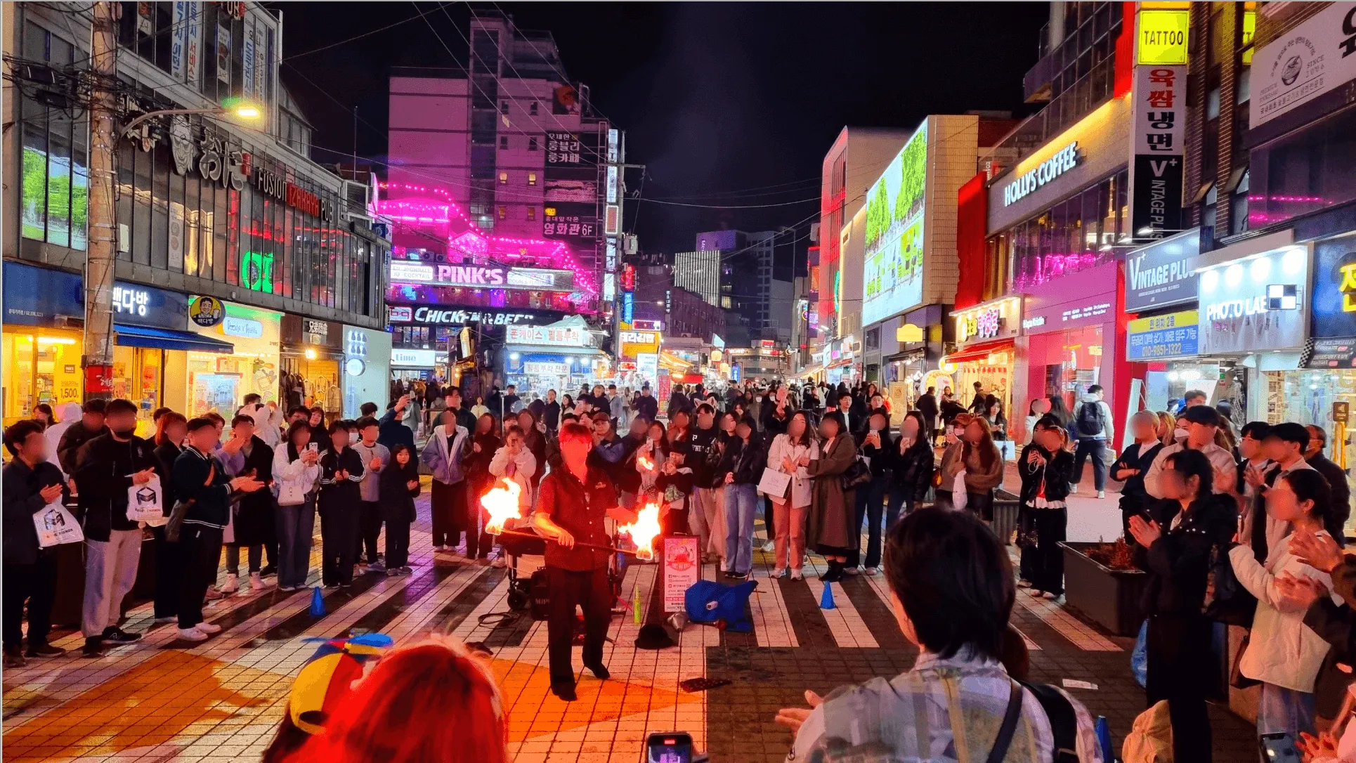 Hongdae street at night with neon signs, crowds, and street performers holding fire props