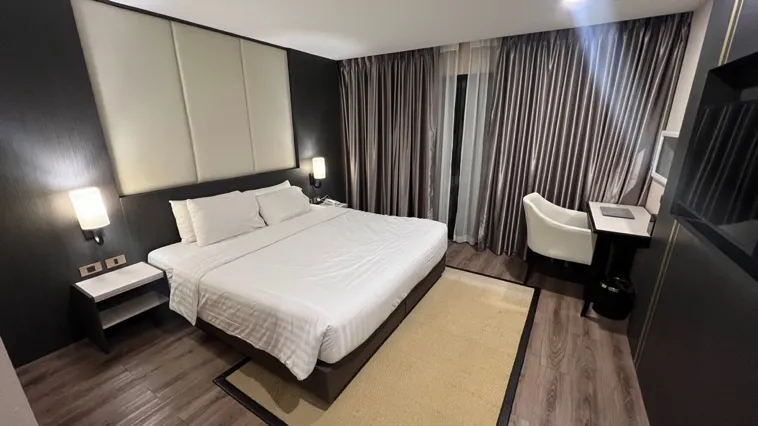 Modern hotel room with king bed, dark accent wall, white bedding, and floor-to-ceiling curtains at Hotel Mayu
