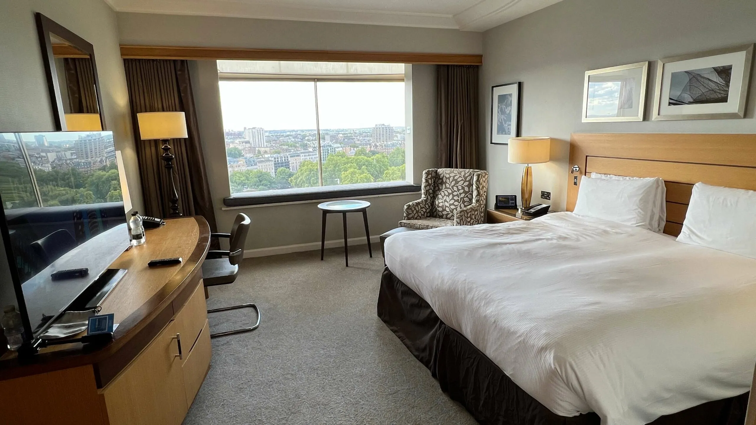 Hotel room with two beds, wood desk, city skyline view from floor-to-ceiling windows.