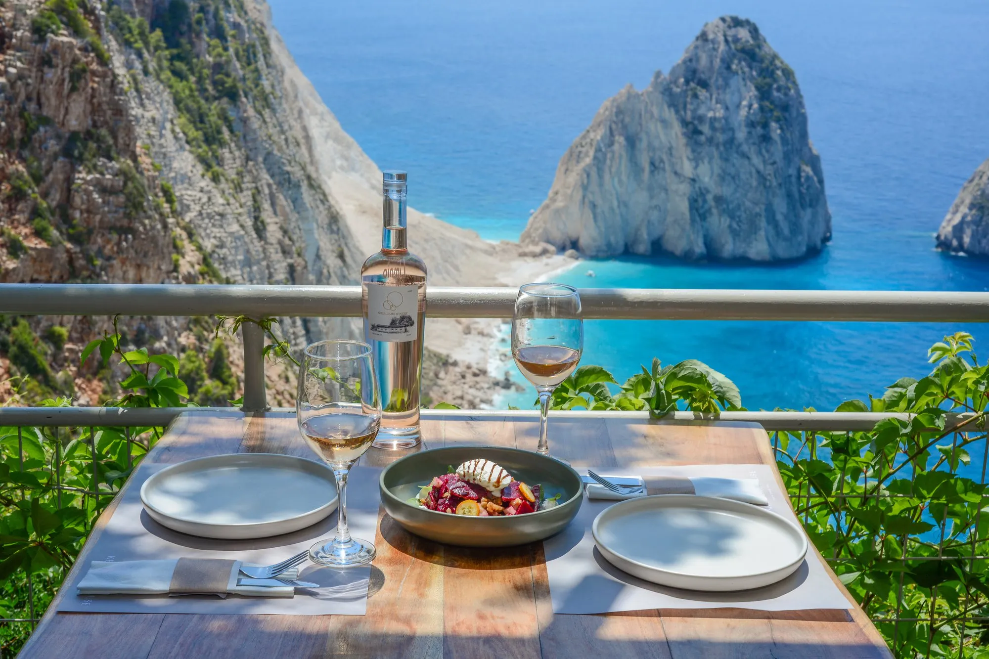 Dining table overlooking Navagio Beach with white wine and a colorful salad bowl, Zakynthos Greece