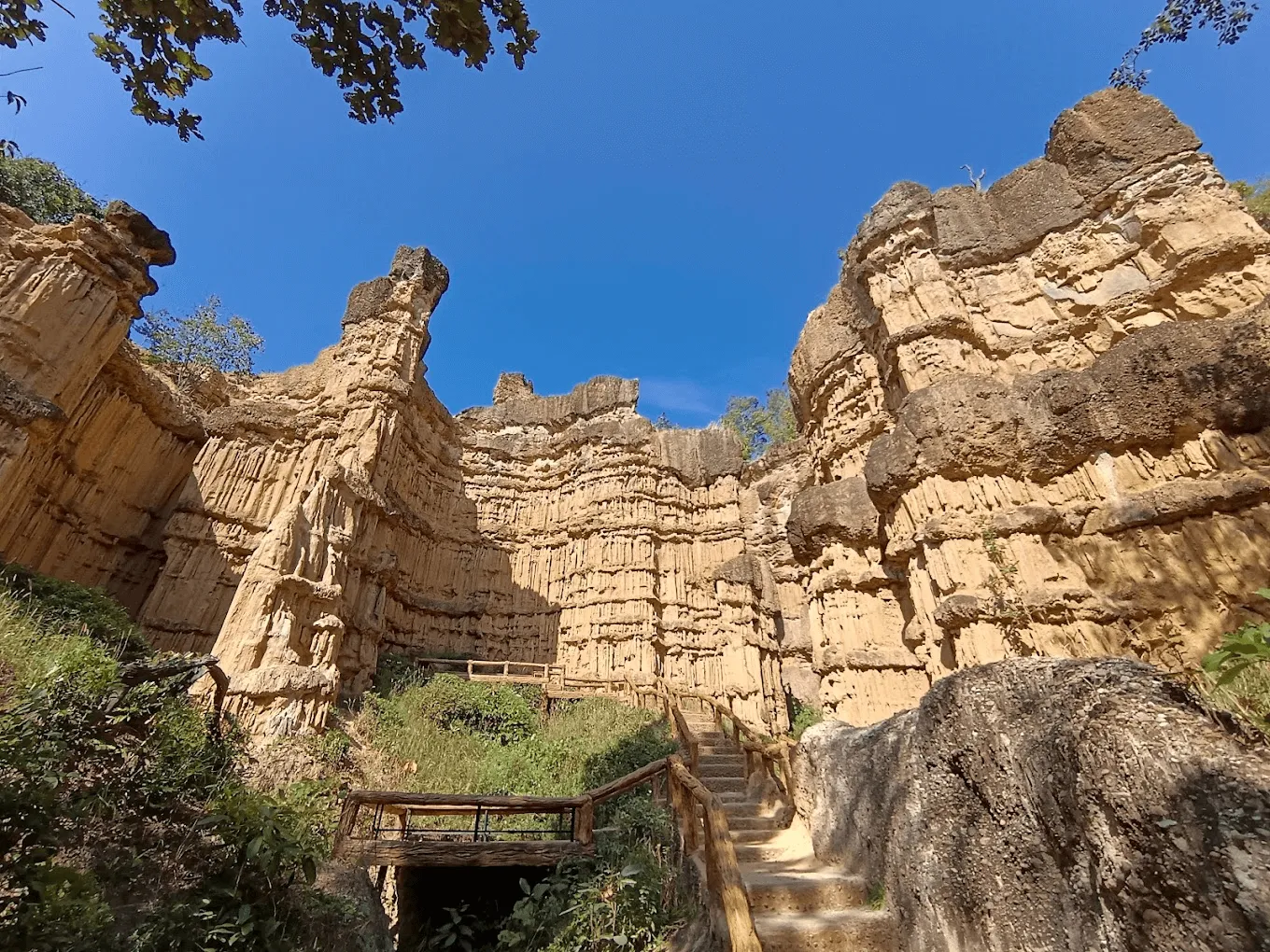Towering columnar basalt rock formations in a canyon with wooden walkways and lush vegetation at Mae Wang, Thailand