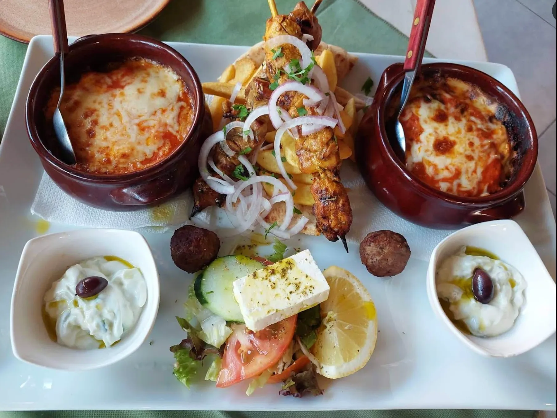 Greek mezze platter with saganaki, grilled lamb skewers, tzatziki, and traditional dips on white plate