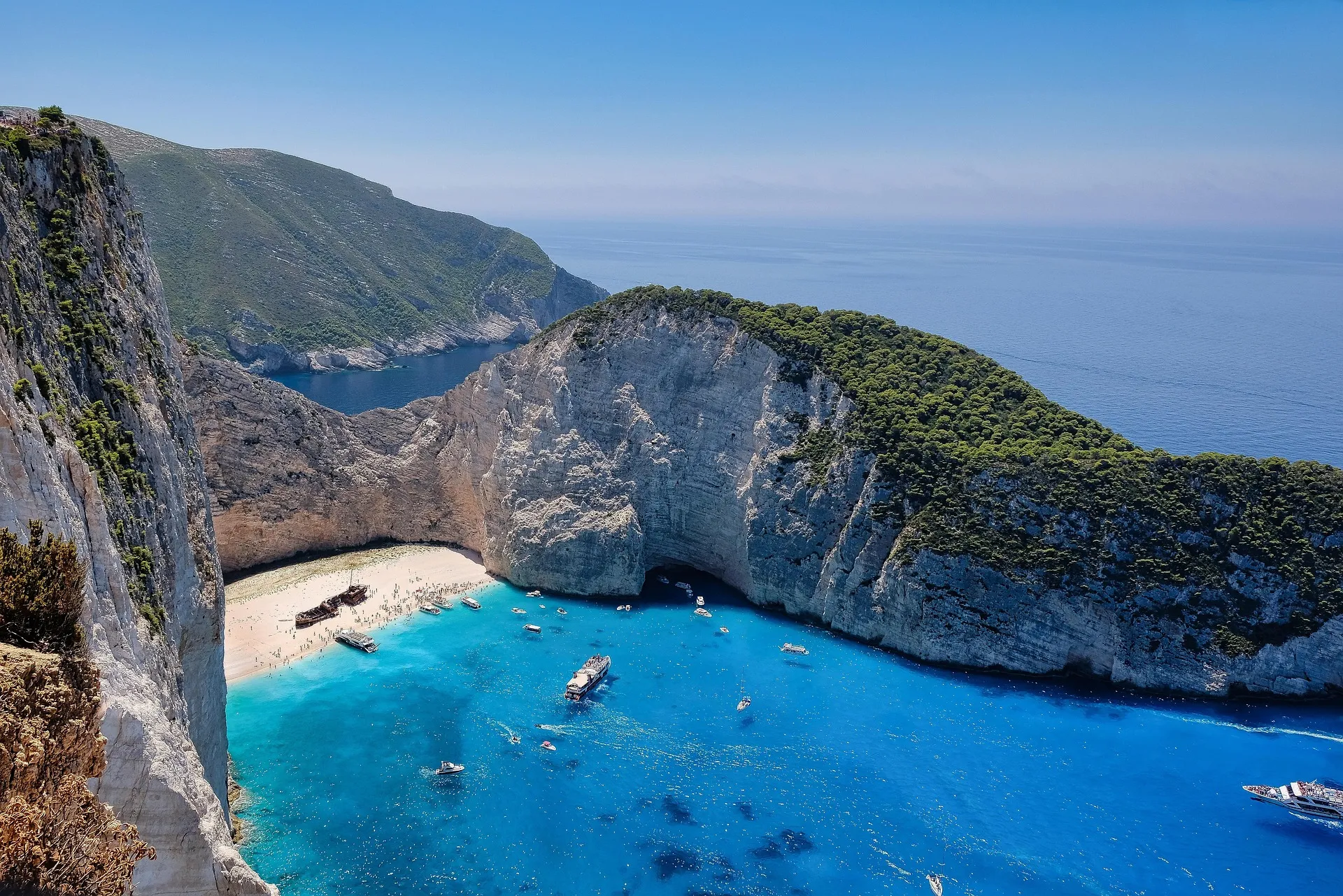 Navagio (Shipwreck) Beach on Zakynthos from the clifftop: white cliffs, turquoise cove, the rusted shipwreck on the sand and tour boats at anchor