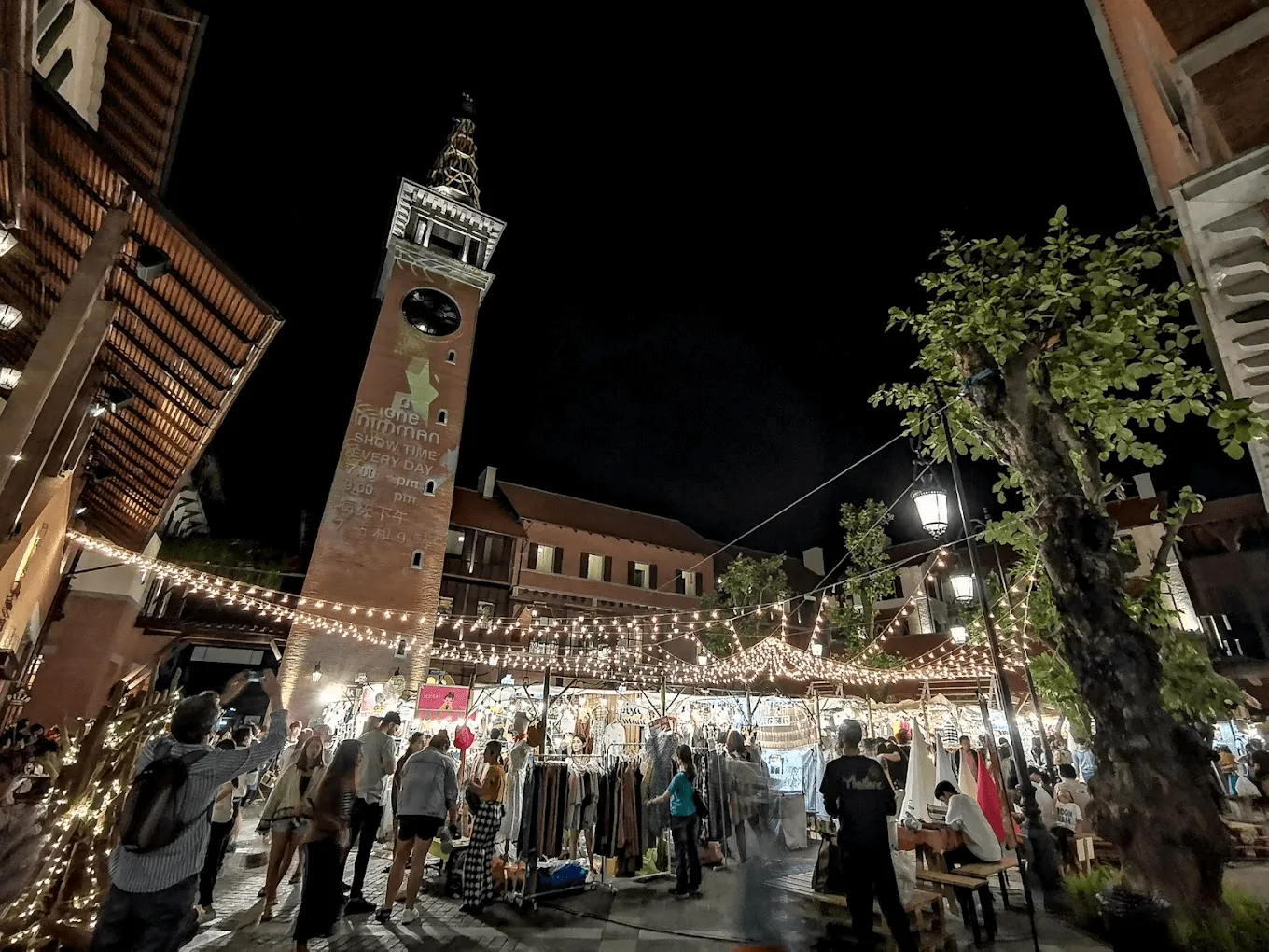 Piazza dei Signori in Vicenza at night with Torre Bissara clock tower, festive string lights, and outdoor market stalls with shoppers