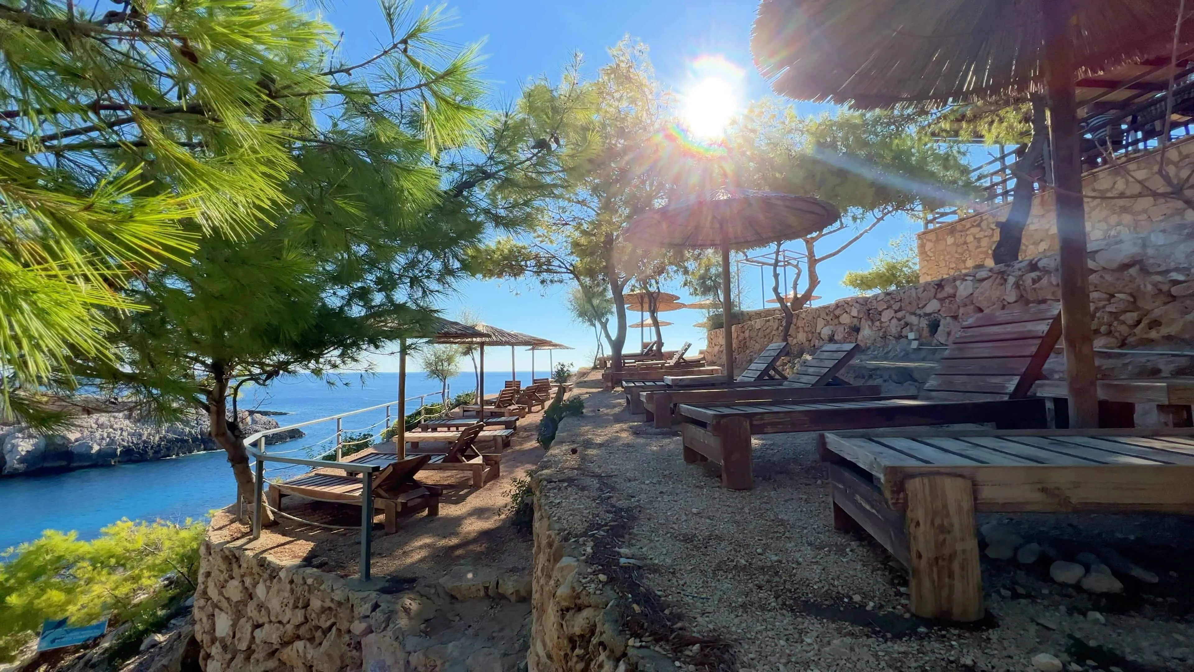 Coastal beach club with wooden sunbeds, thatch umbrellas, and turquoise Mediterranean waters at Port Limnionas