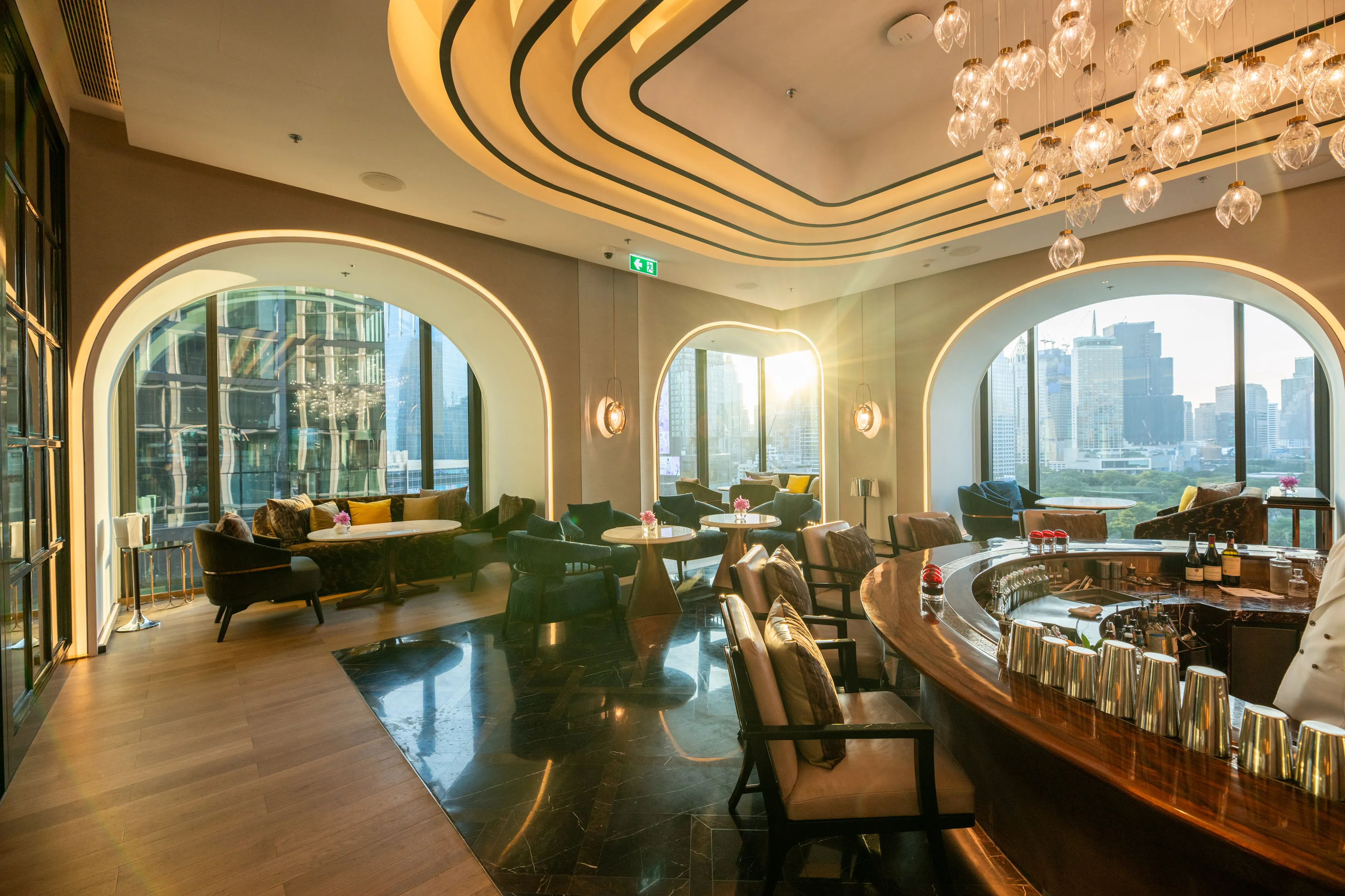 Ritz-Carlton Bangkok lounge with curved archways, green velvet seating, modern ceiling details, and cityscape views through floor-to-ceiling windows