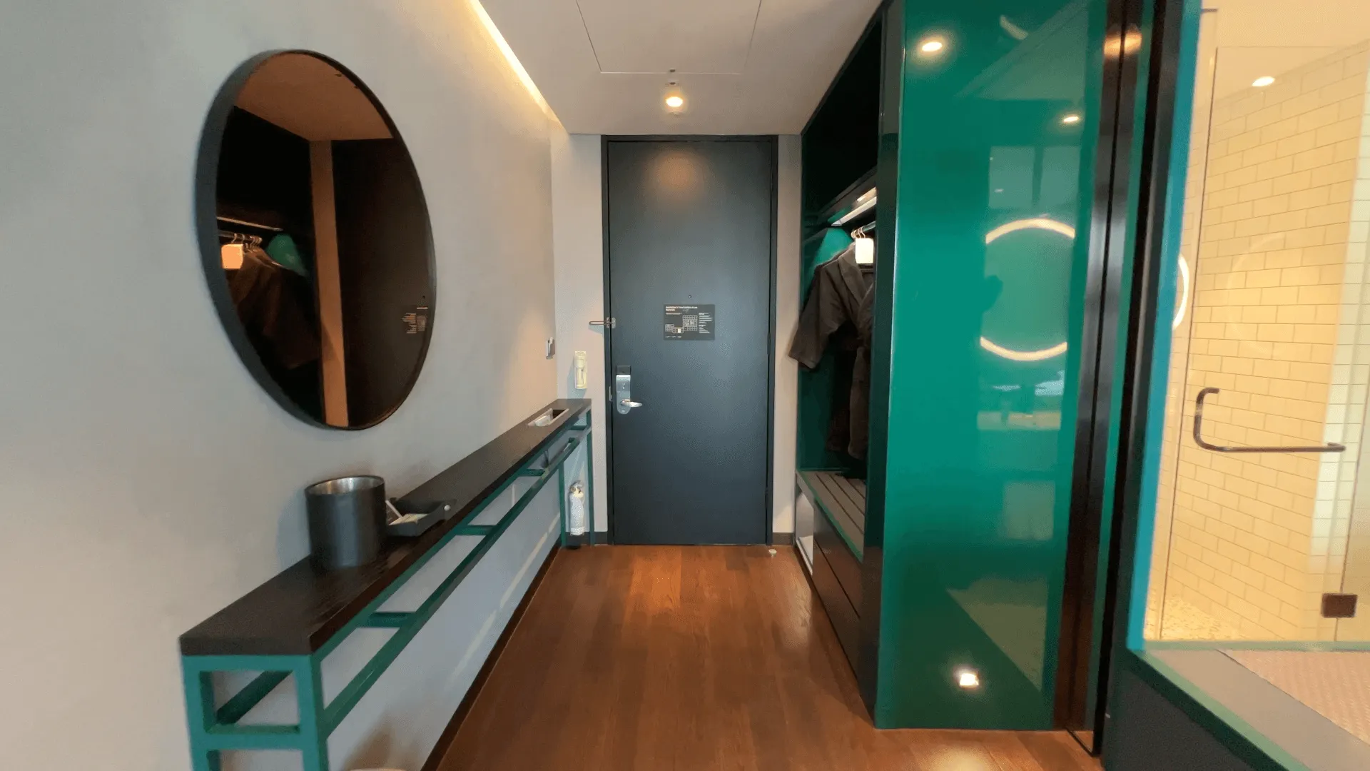 Modern hotel foyer with teal and white design, oval mirror, dark door, and wood flooring at Ryse Hotel