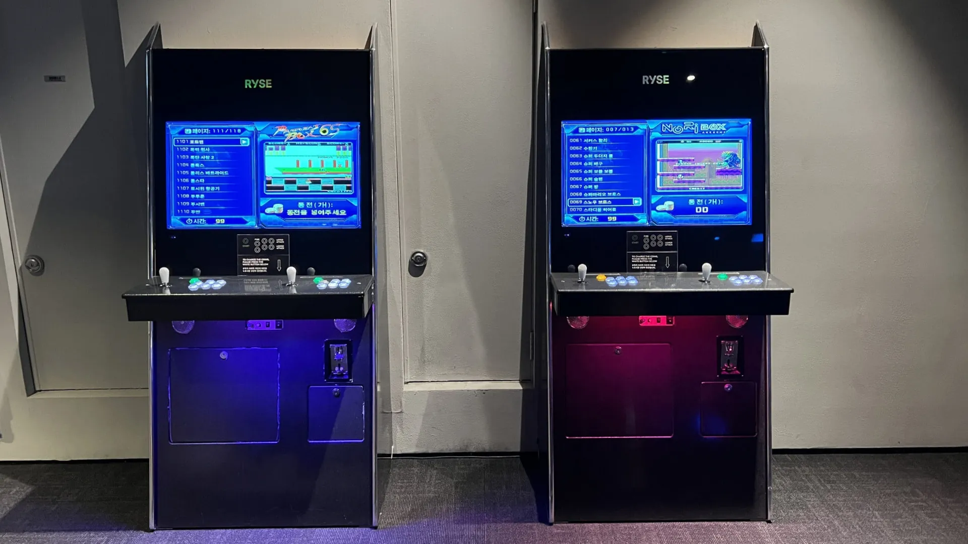 Two RYSE arcade game cabinets with blue and purple illuminated screens in an airport terminal.