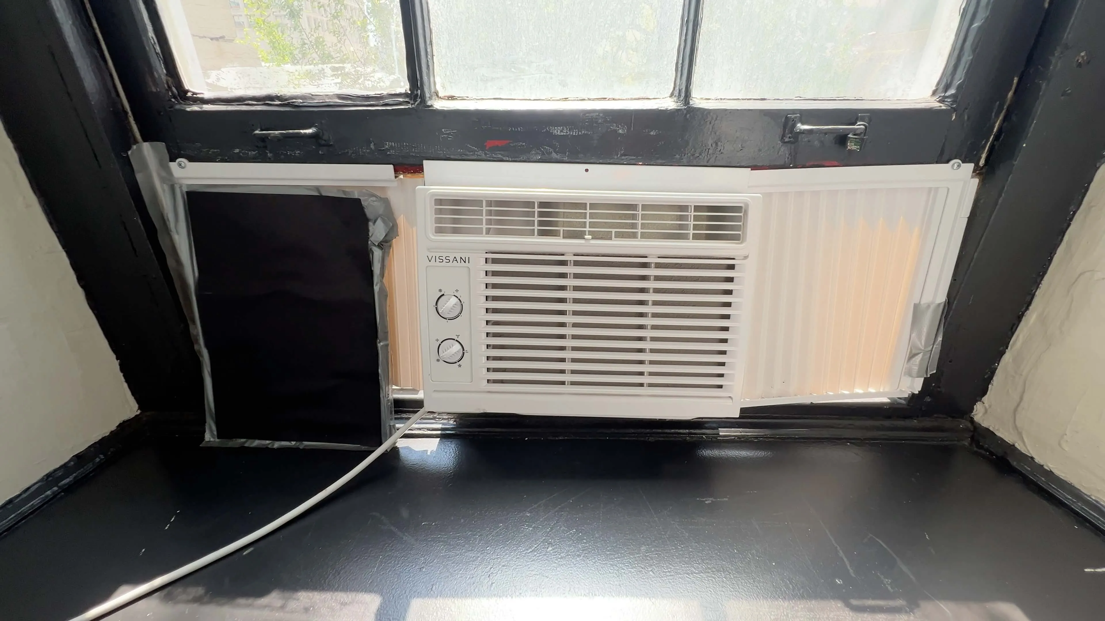 Window-mounted Vissani air conditioner unit in a hotel room with black-framed window and dark sill.