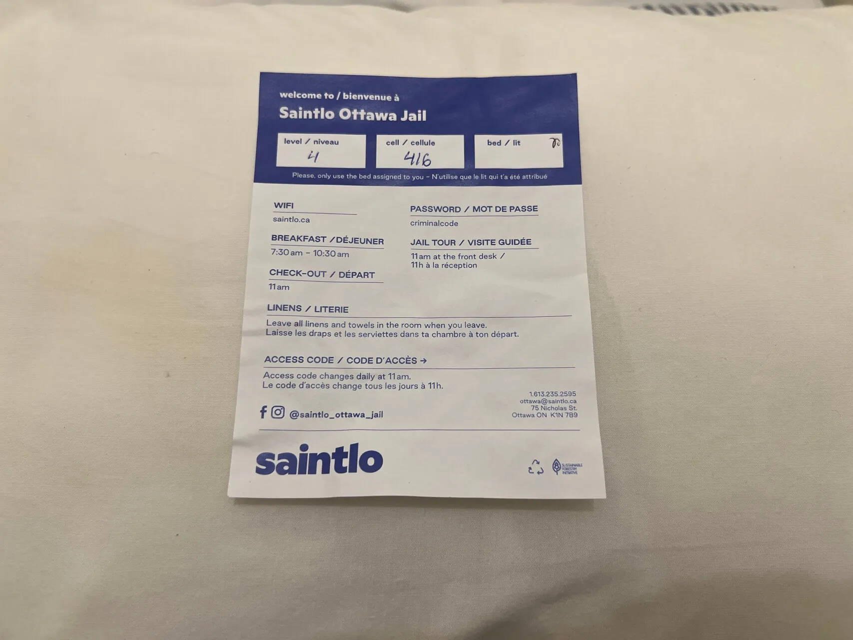 Saintlo Ottawa Jail hotel welcome card with room details, WiFi, breakfast times, and check-out information on white bedding