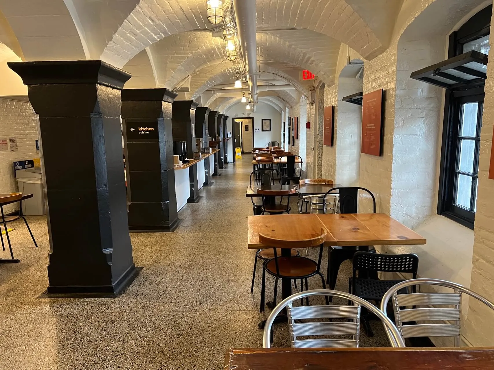 Modern dining area with arched brick ceilings, wooden tables, metal chairs, and black service counters in a converted heritage stone building